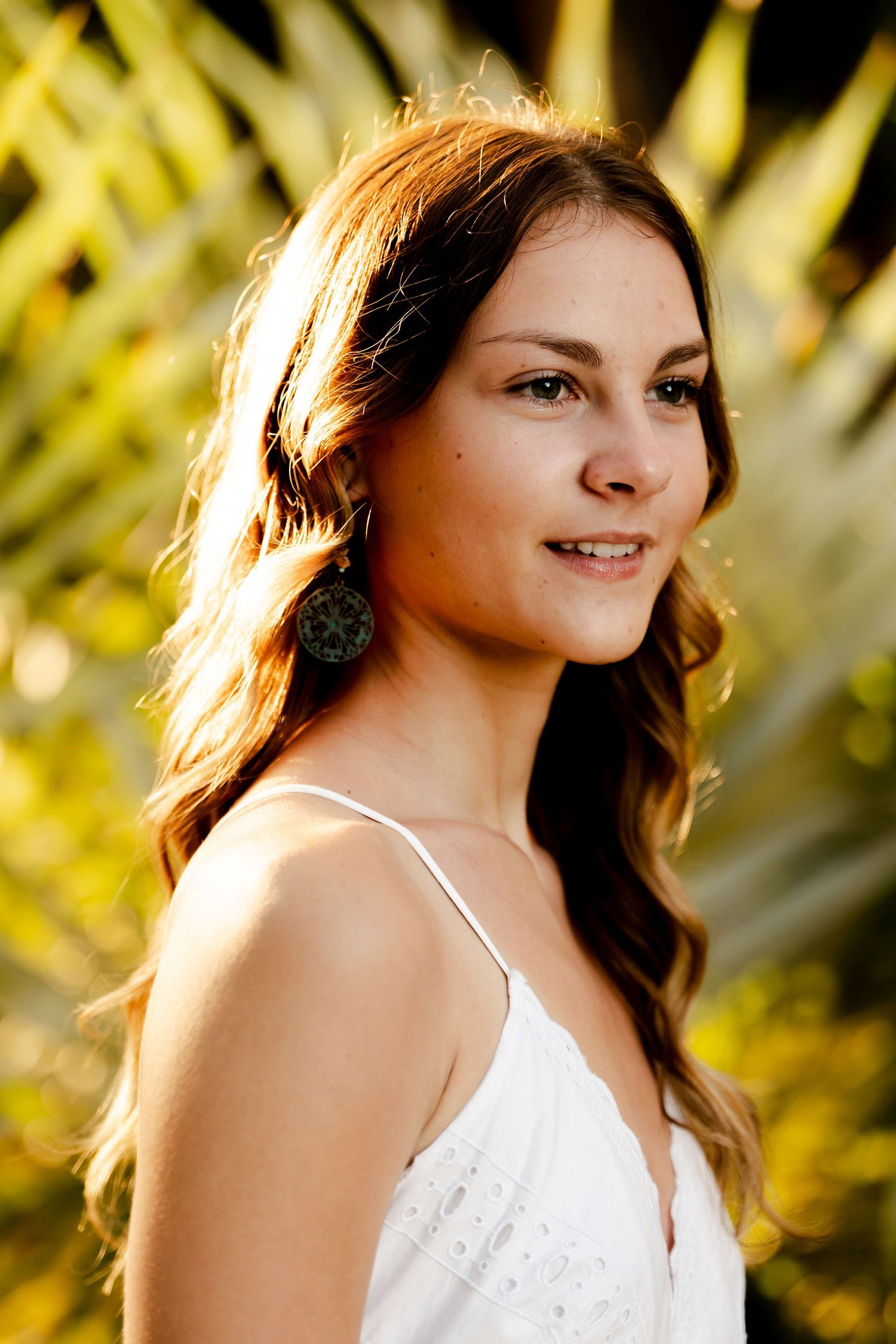 Portrait of woman in white dress with earrings against tropical foliage background.