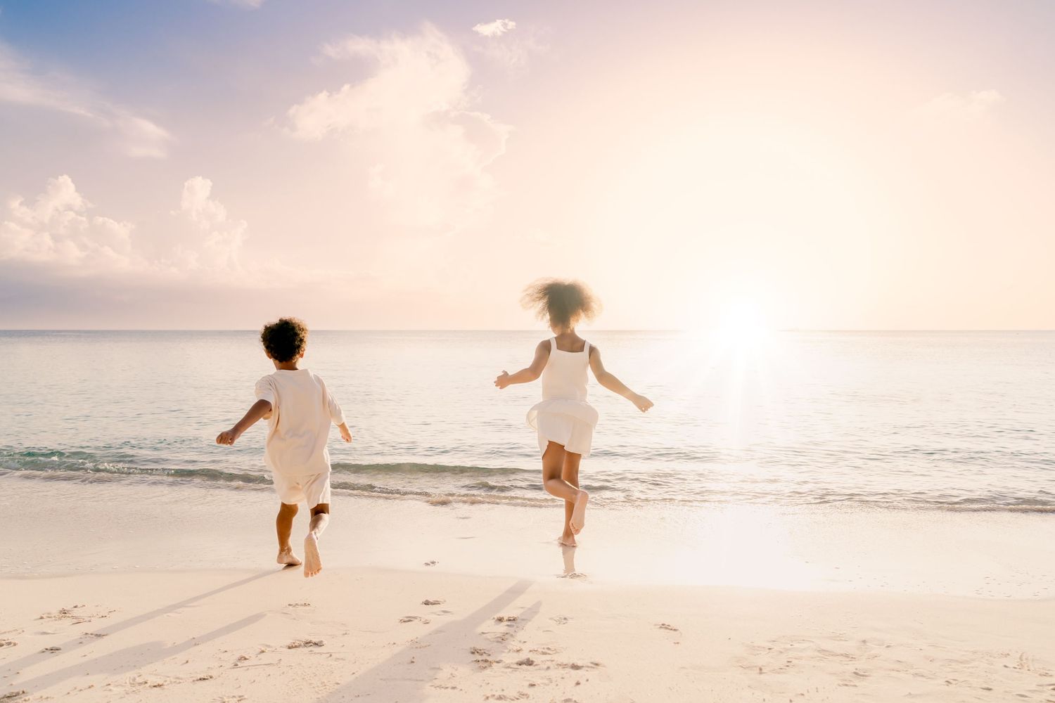 Two people run joyfully along a beach at sunset creating silhouettes against the sky.
