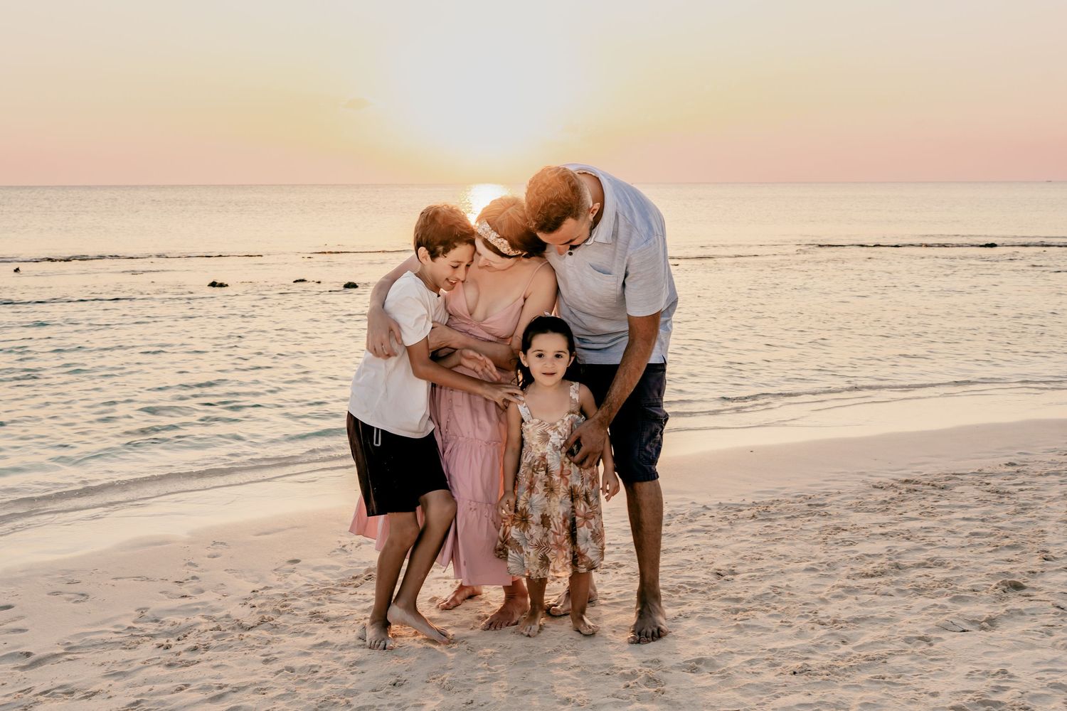 Beautiful beach family photoshoot with everyone kneeling in the sand at sunset.
