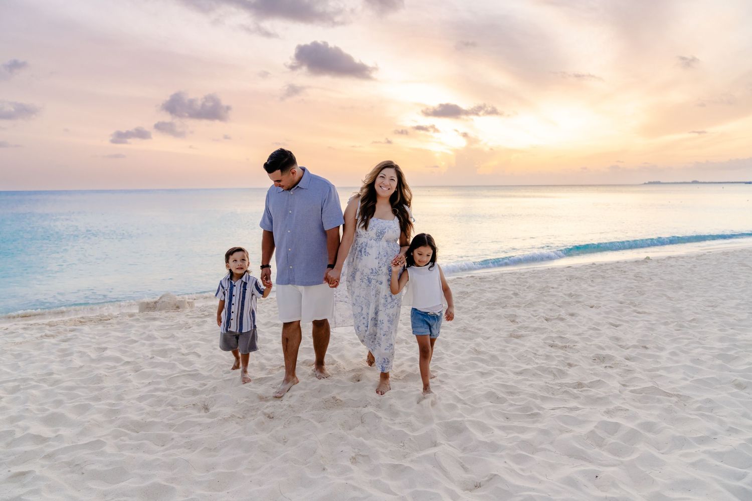 Family members stroll together on a beautiful beach at sunset wearing coordinated white and neutral outfits.