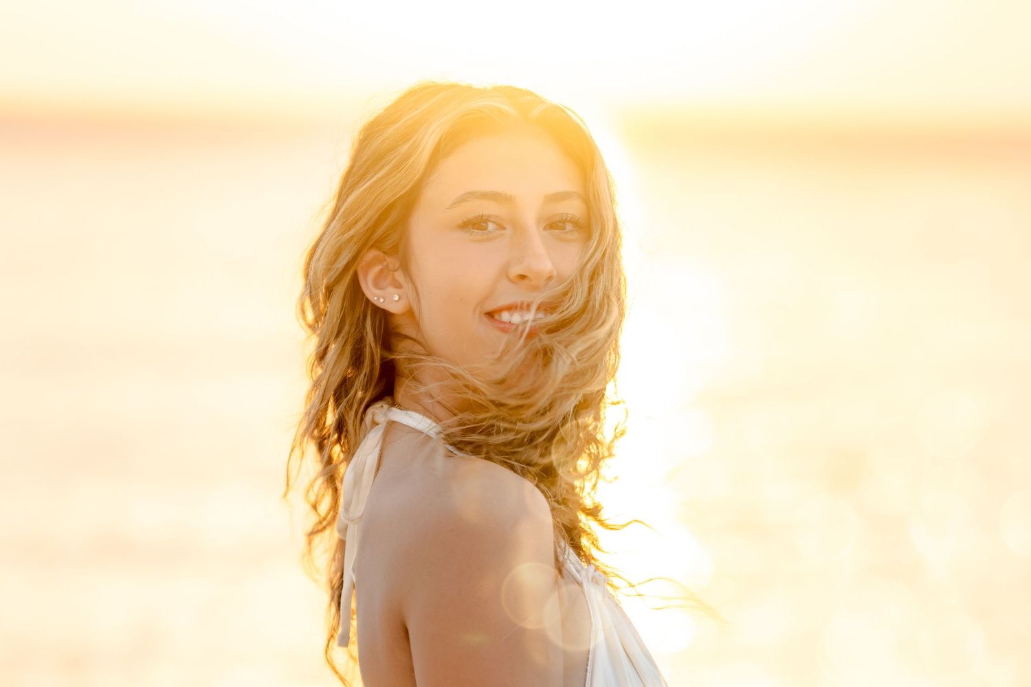 Woman with windswept hair in golden sunset light at beach.