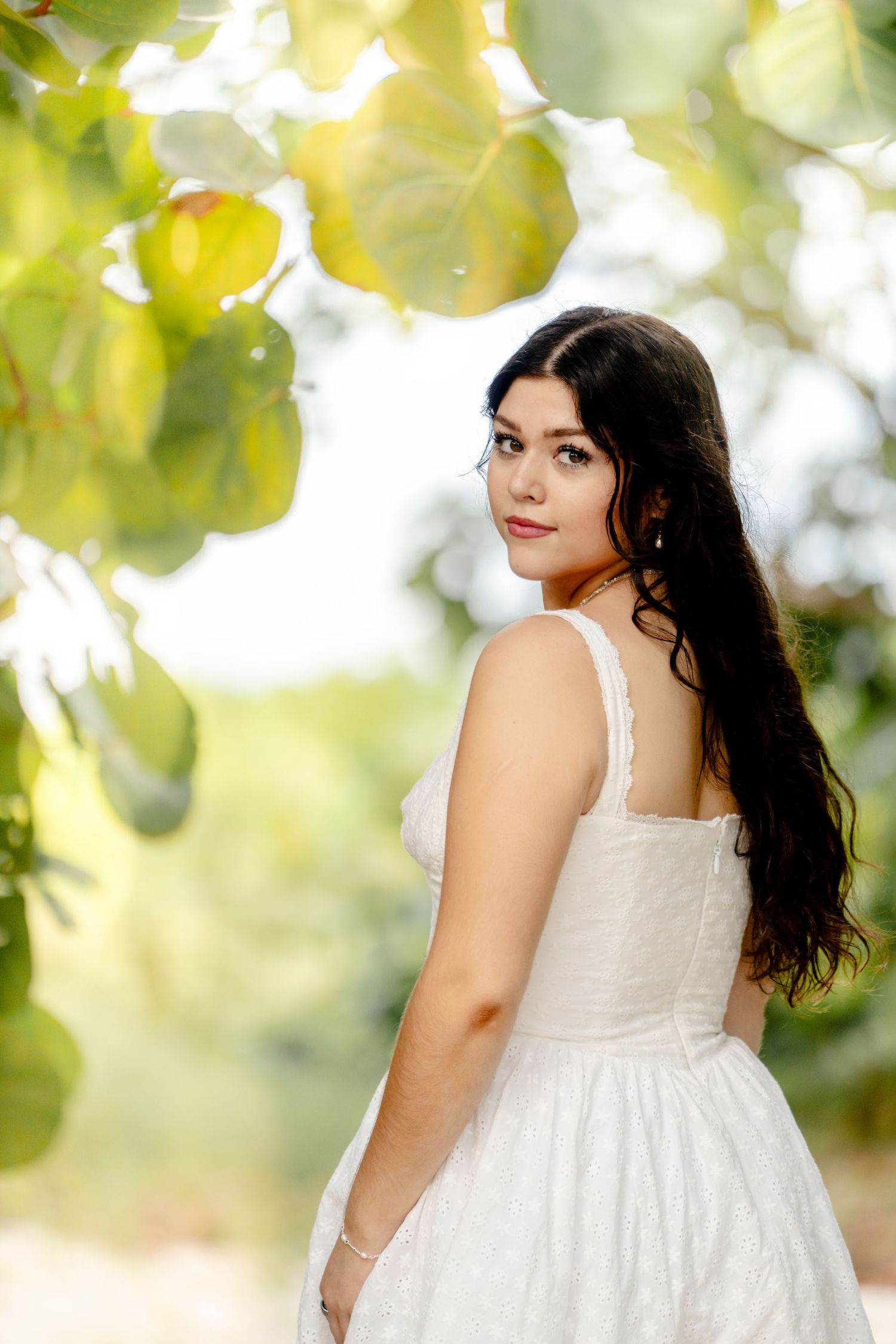 Sunlit garden photoshoot with white dress against bright green leaves.