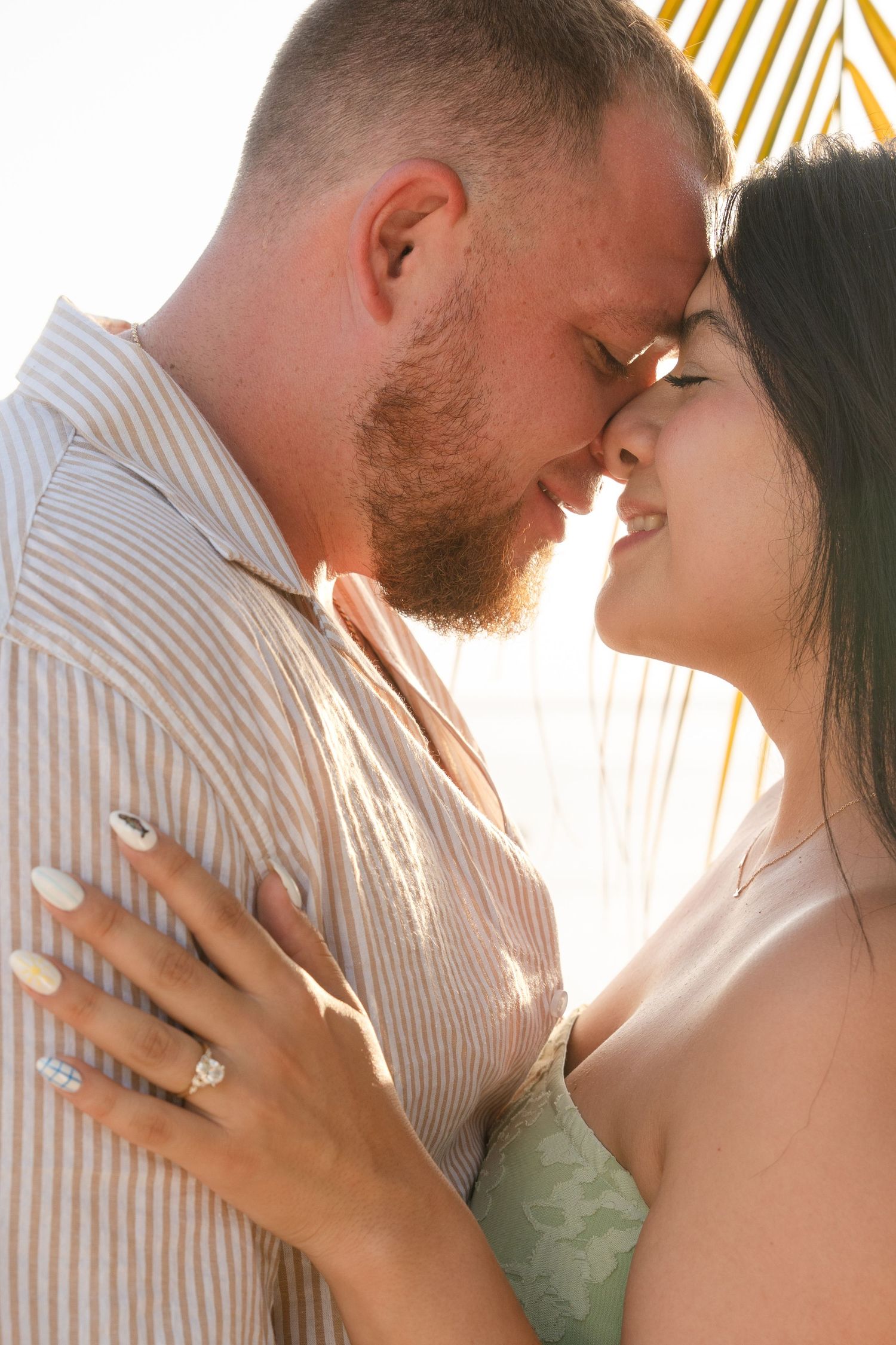 Couple sharing a romantic moment outdoors, woman wearing an engagement ring, backlit by warm golden sunlight.