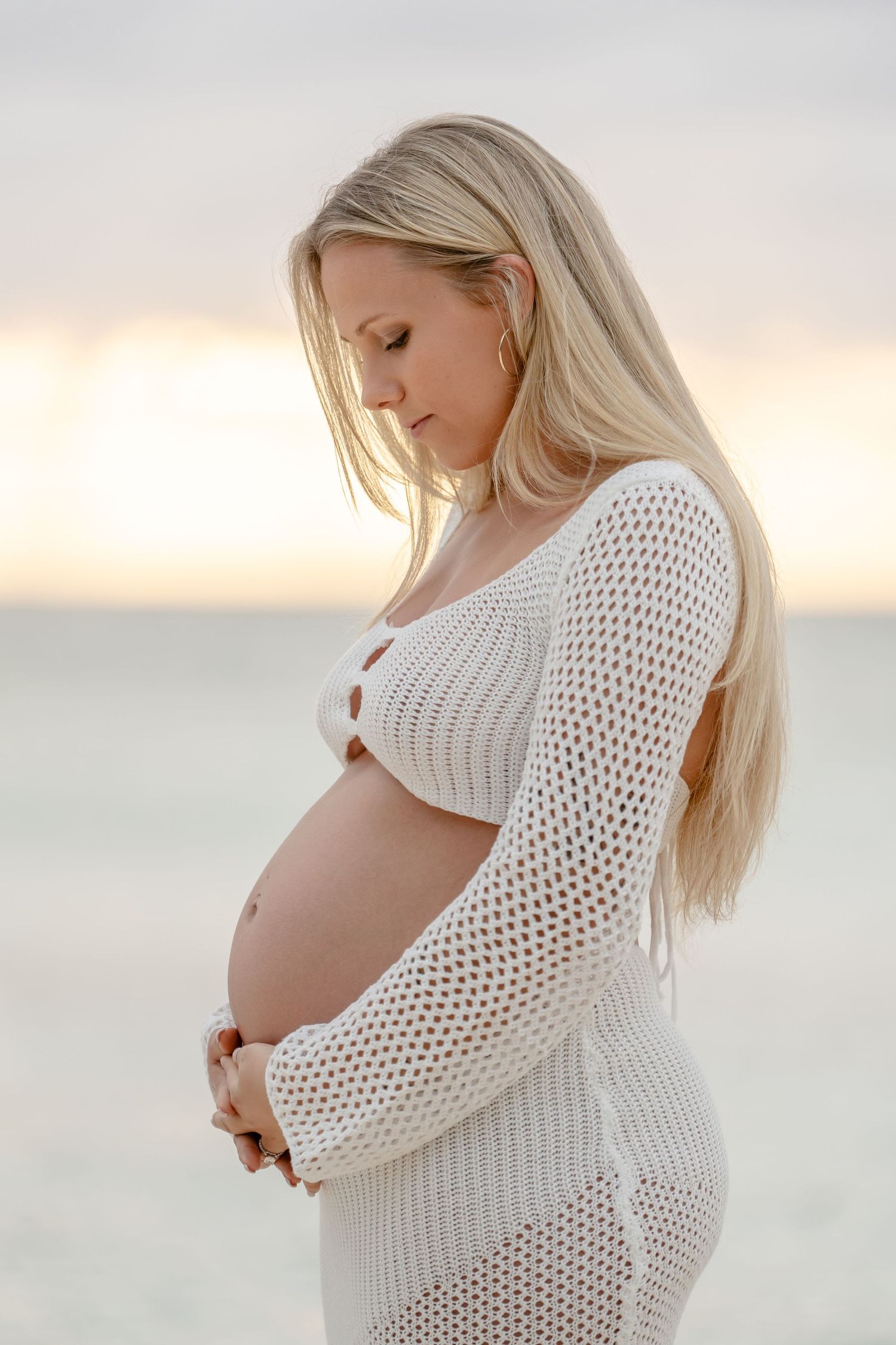 Serene beach maternity portraits featuring person in white crochet dress against ocean backdrop.