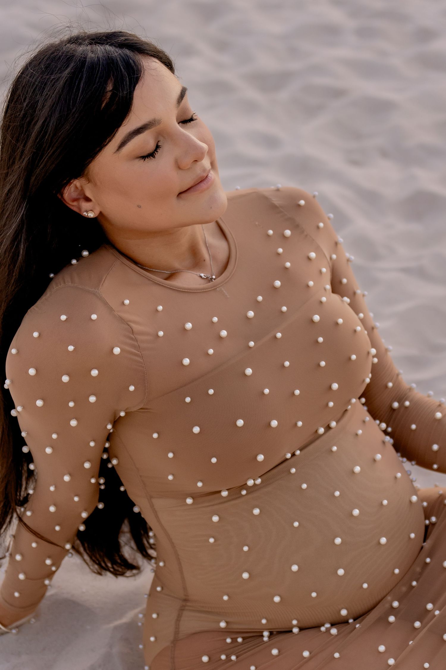 Expecting mother wearing polka dot dress poses on sandy beach during photoshoot.