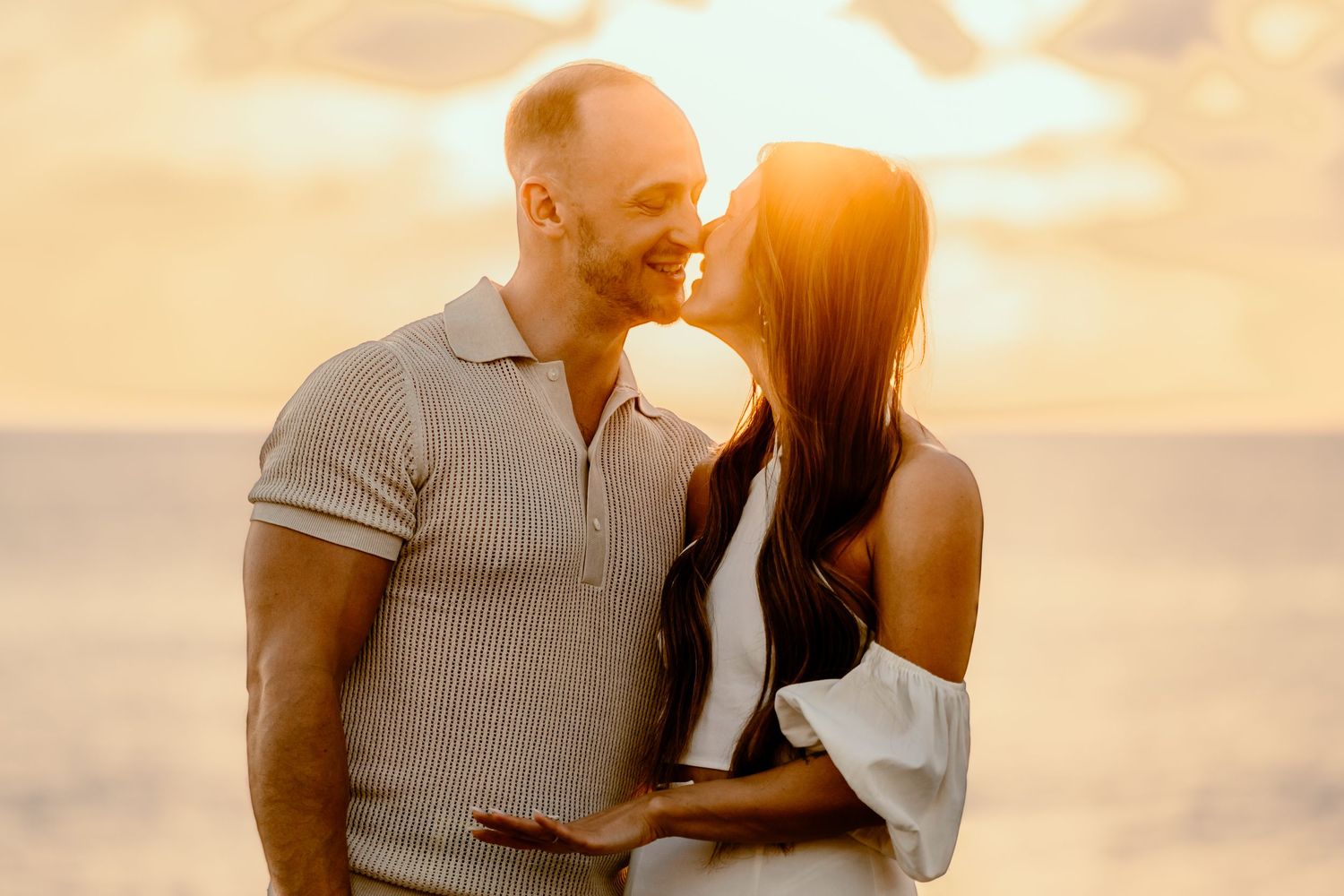 A loving couple sharing a tender moment against a golden sunset backdrop over the ocean.