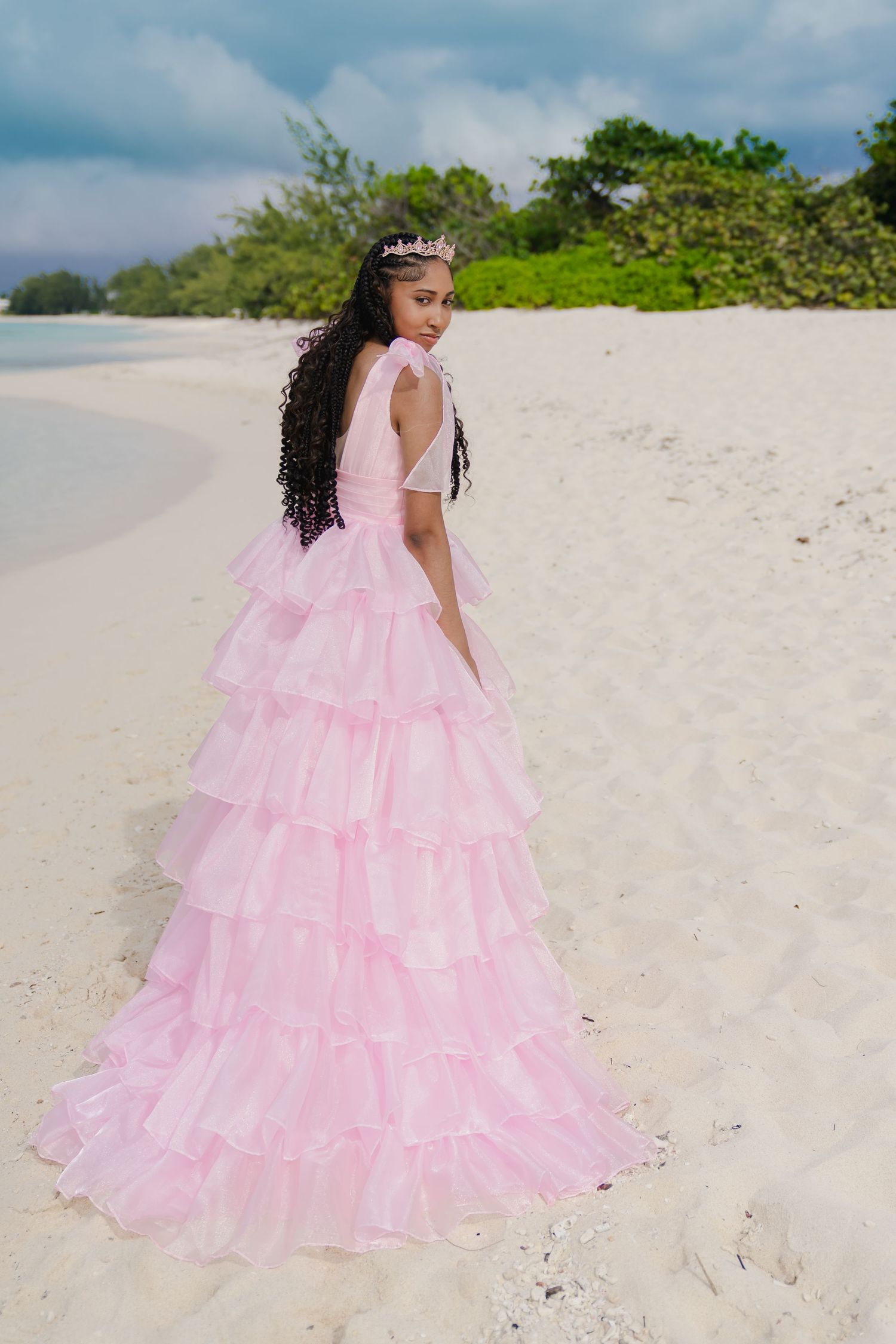 Person in pink ruffled gown walking along white sandy beach.