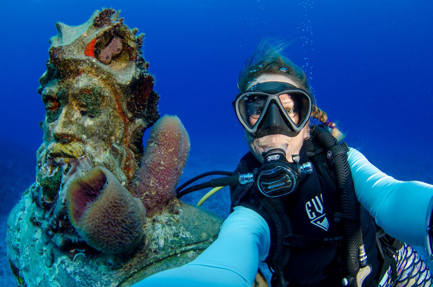 Scuba diver explores vibrant coral reef with schools of tropical fish swimming in crystal blue waters.