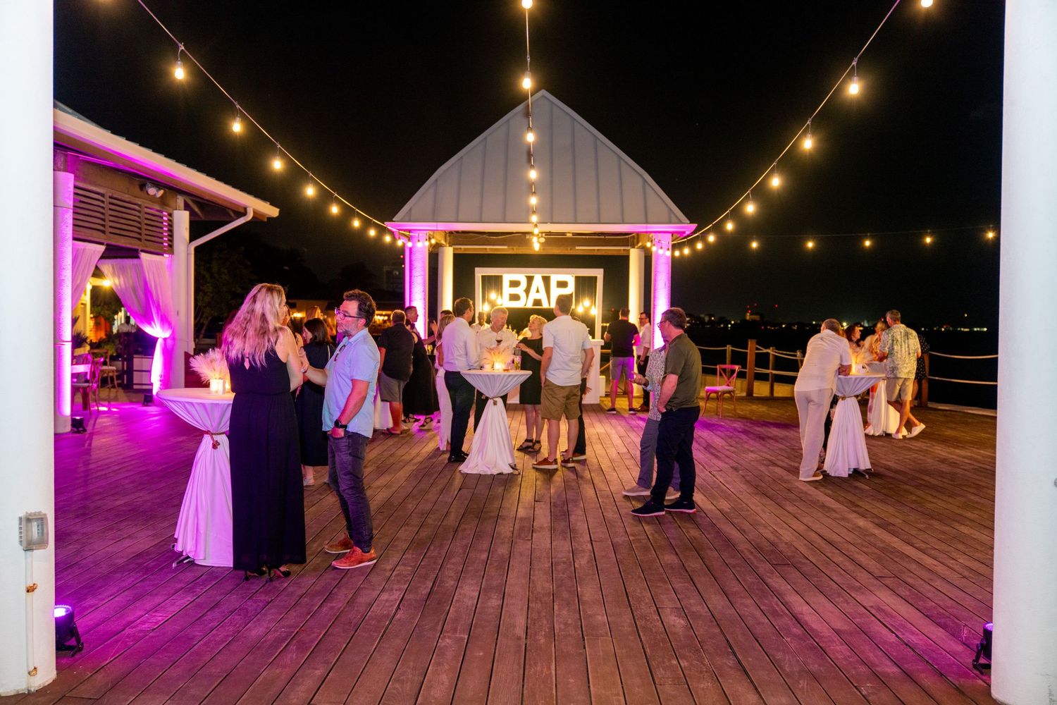 Wedding reception on a deck with string lights and pink uplighting creating a romantic atmosphere.