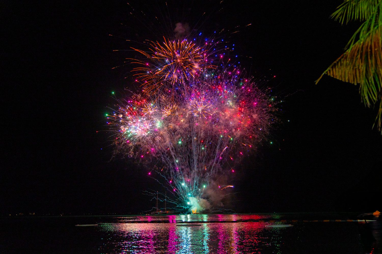 Dazzling fireworks illuminate the night sky with pink and green sparkles mirrored in the water below.