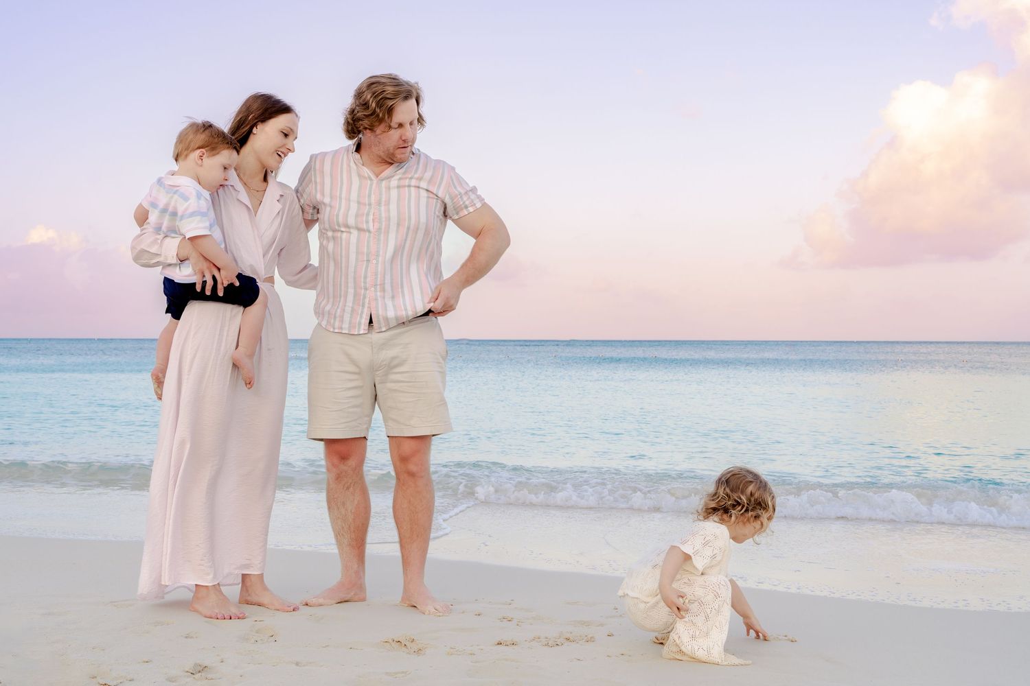 Family dressed in white enjoying a sunset photoshoot on a pristine beach.