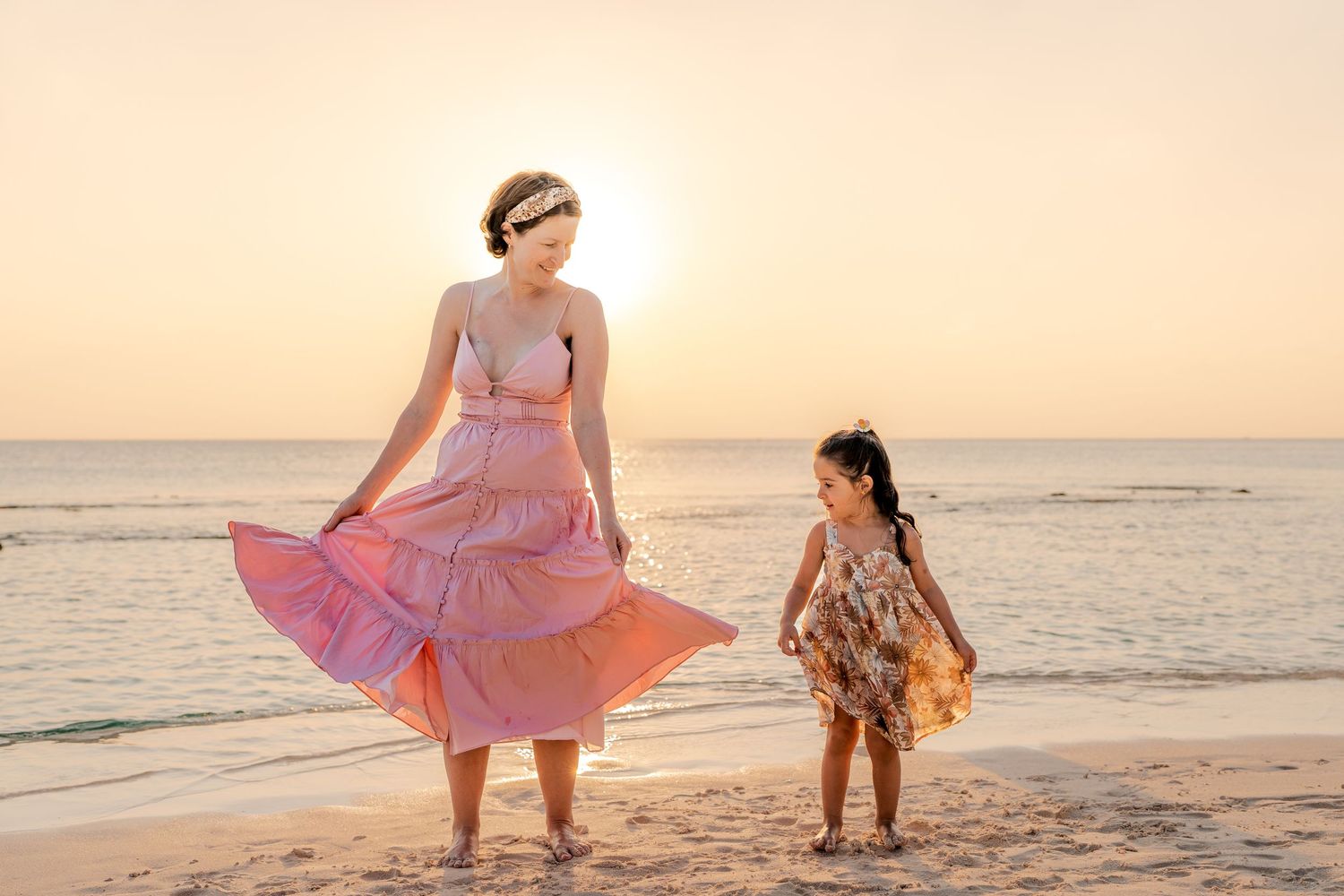 Playful beach photography session with flowing dresses against a sunset backdrop.