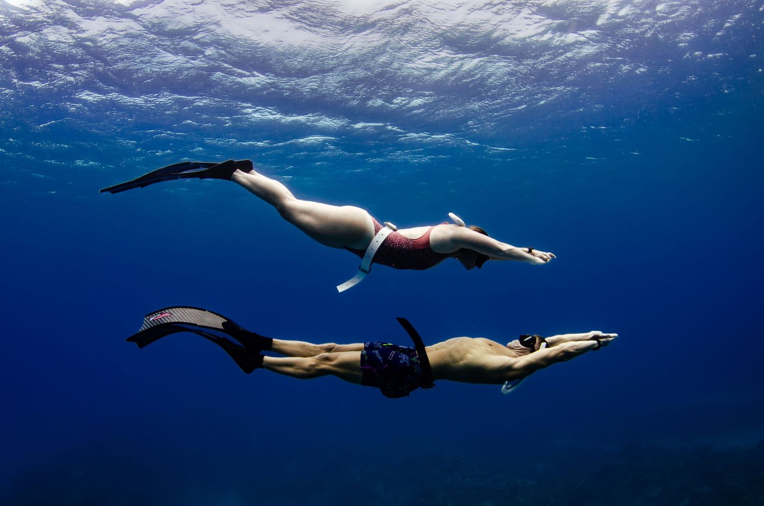 Two snorkelers gliding through deep blue ocean waters with fins.