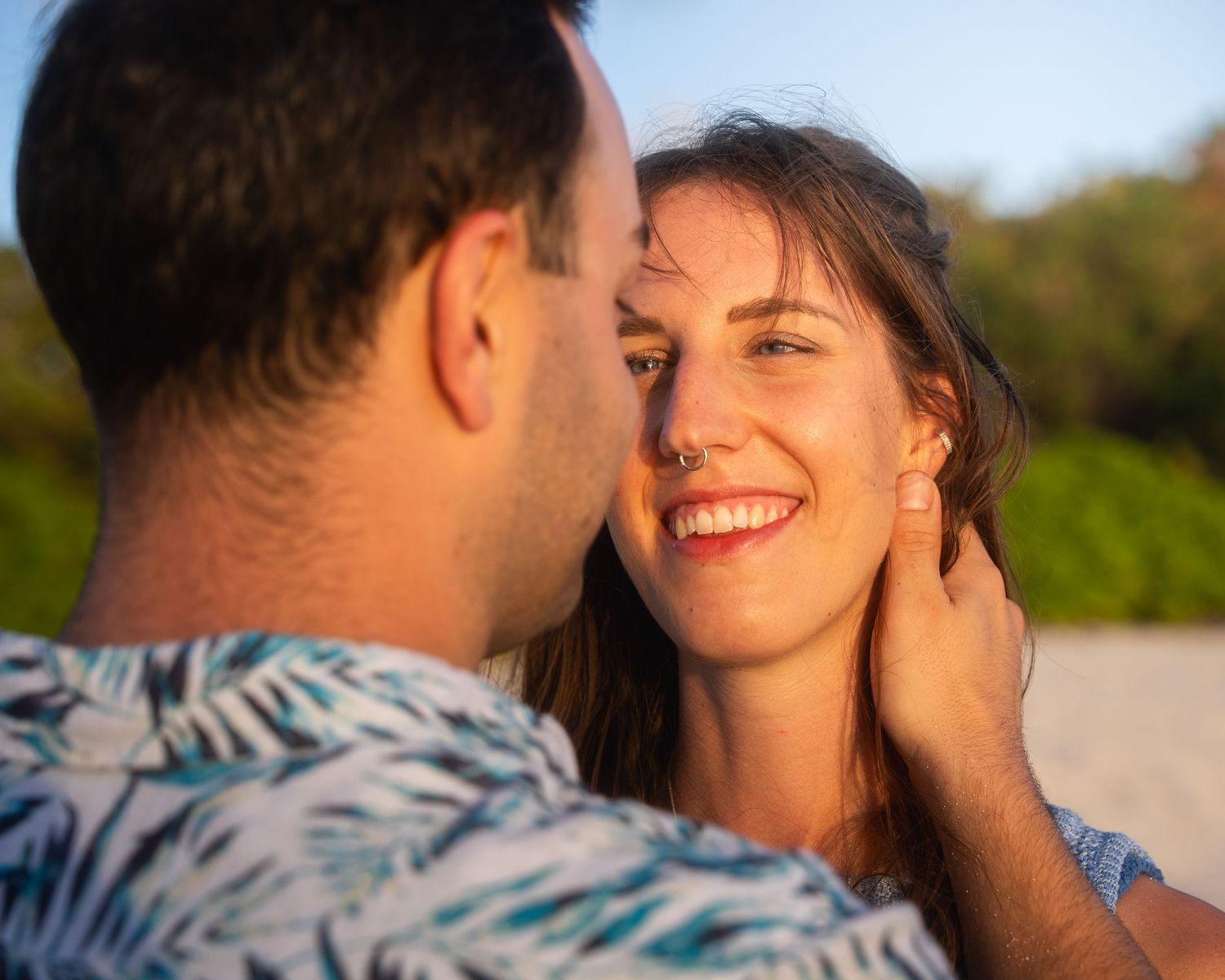 Romantic couple moment on beach, man tenderly holding womans face as she smiles.