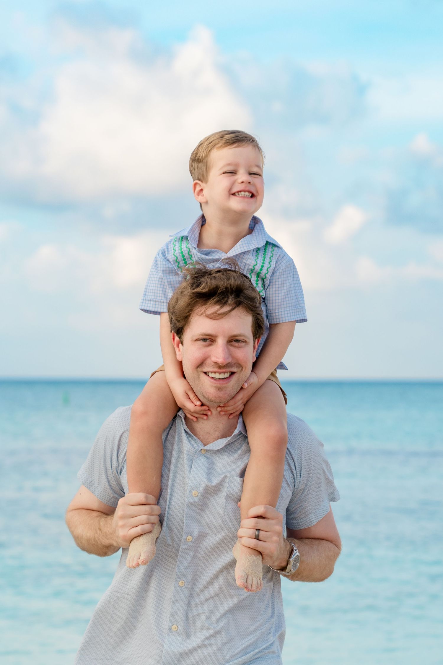 Joyful parent and child playing together on a sunny beach with turquoise ocean waters in the background.
