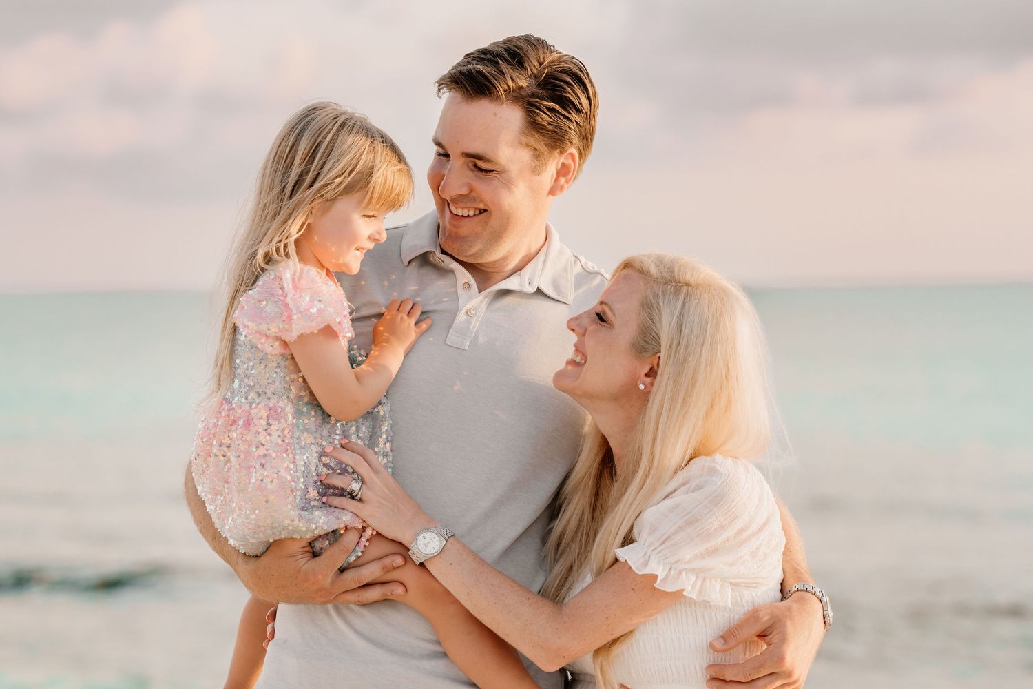 Candid family moments shared on a beach with soft pastel sunset colors.