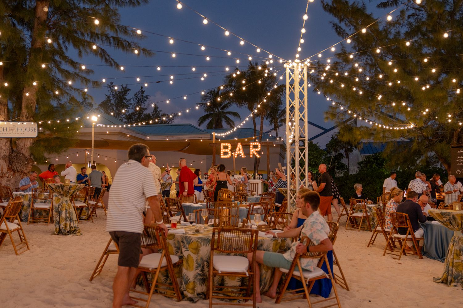 Outdoor evening dining area with string lights creating a warm ambiance under palm trees.