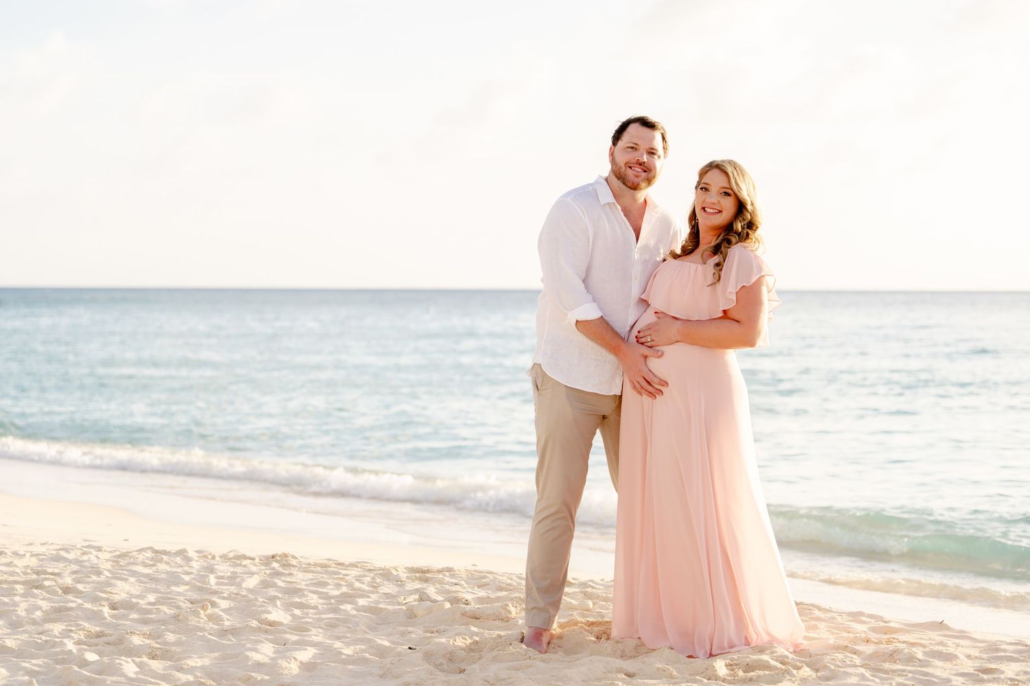 Loving couple poses together on sandy beach with ocean waves in background during golden hour.