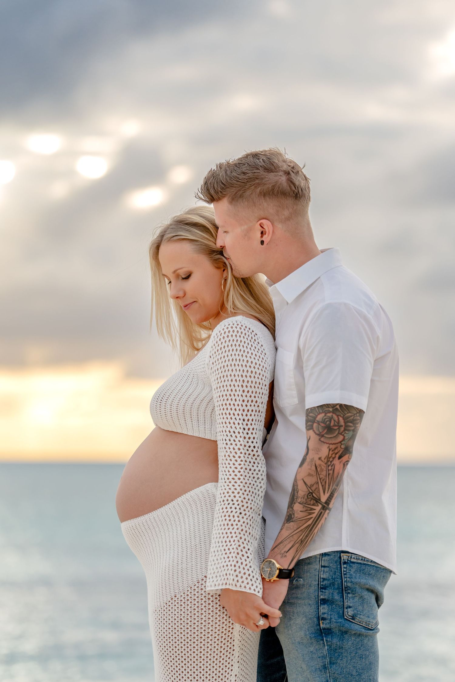 Romantic beachside maternity photos with couple embracing during sunset.