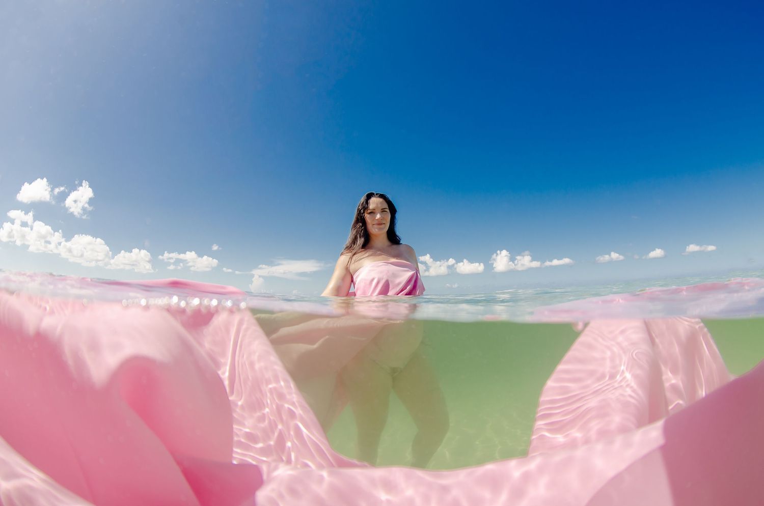Flowing pink fabric billows against bright blue sky with white clouds on a sunny day.