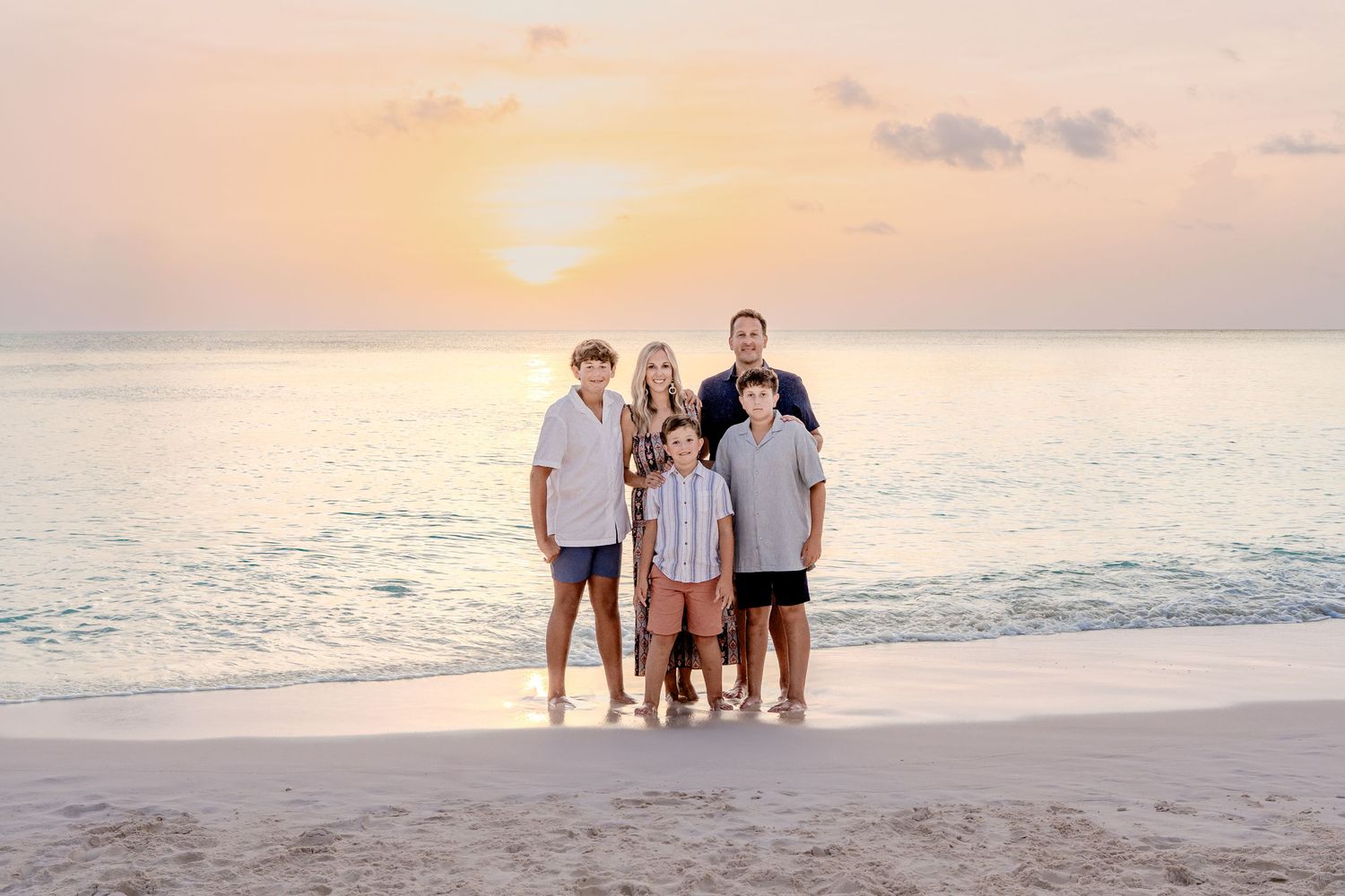 Family beach photography session with warm sunset lighting and gentle waves in the background.