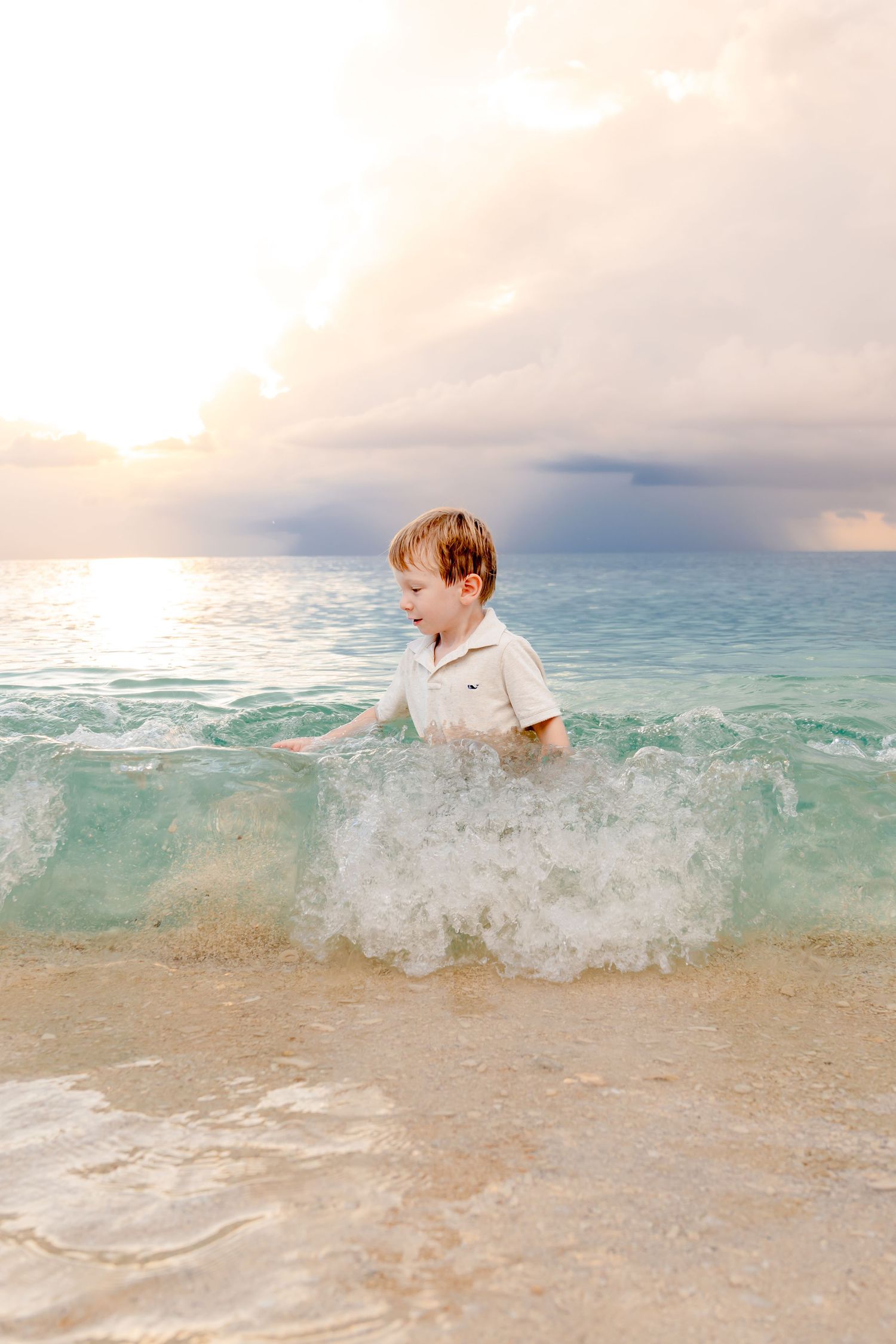 Child playing in crystal clear ocean waves during sunset with splashing water.