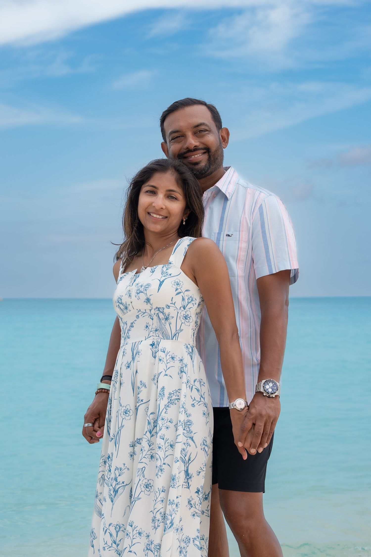 Happy couple posing on a tropical beach with turquoise ocean water and blue sky backdrop.