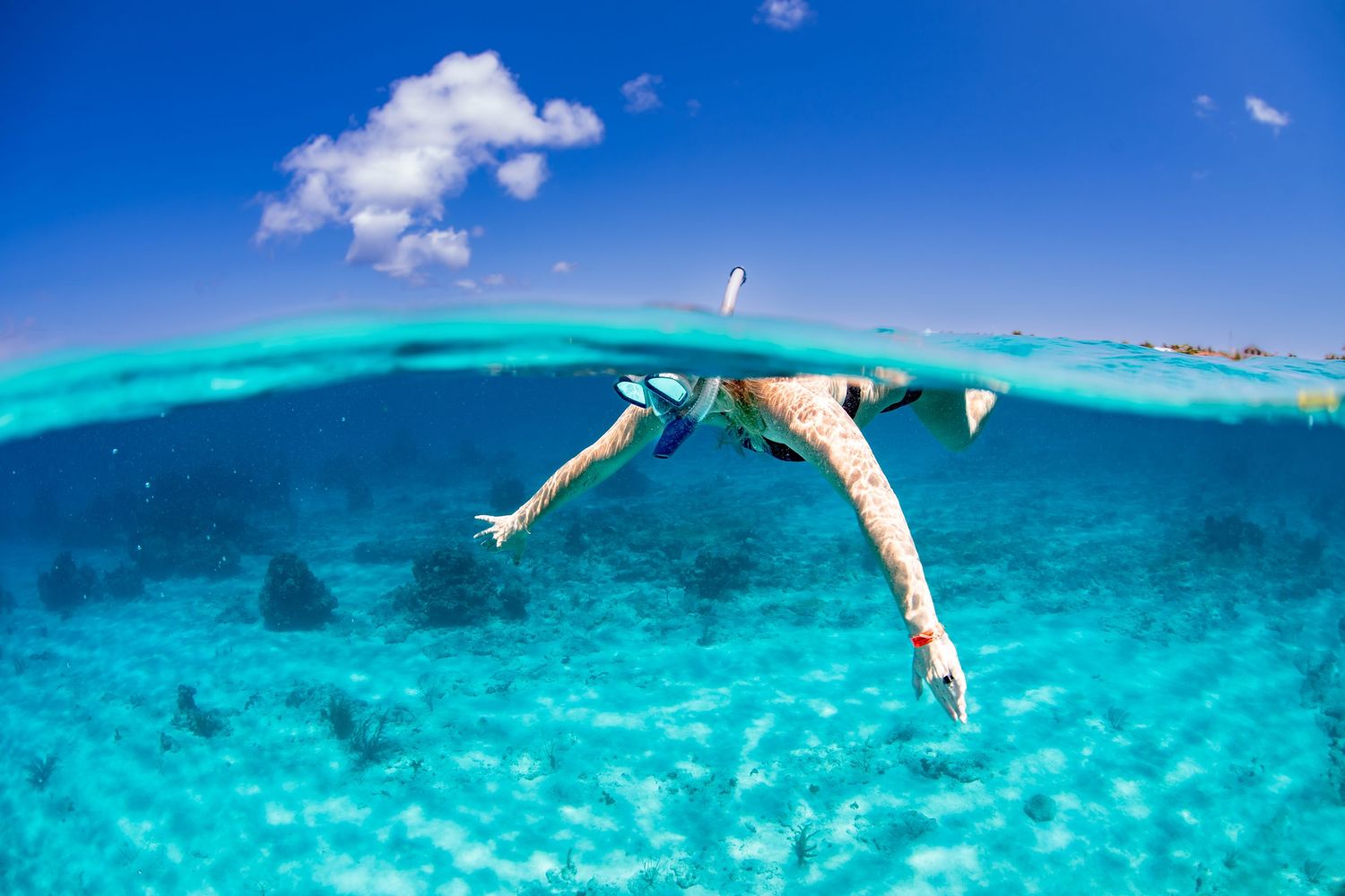 Split-shot underwater photo of swimmer diving in crystal clear tropical waters.