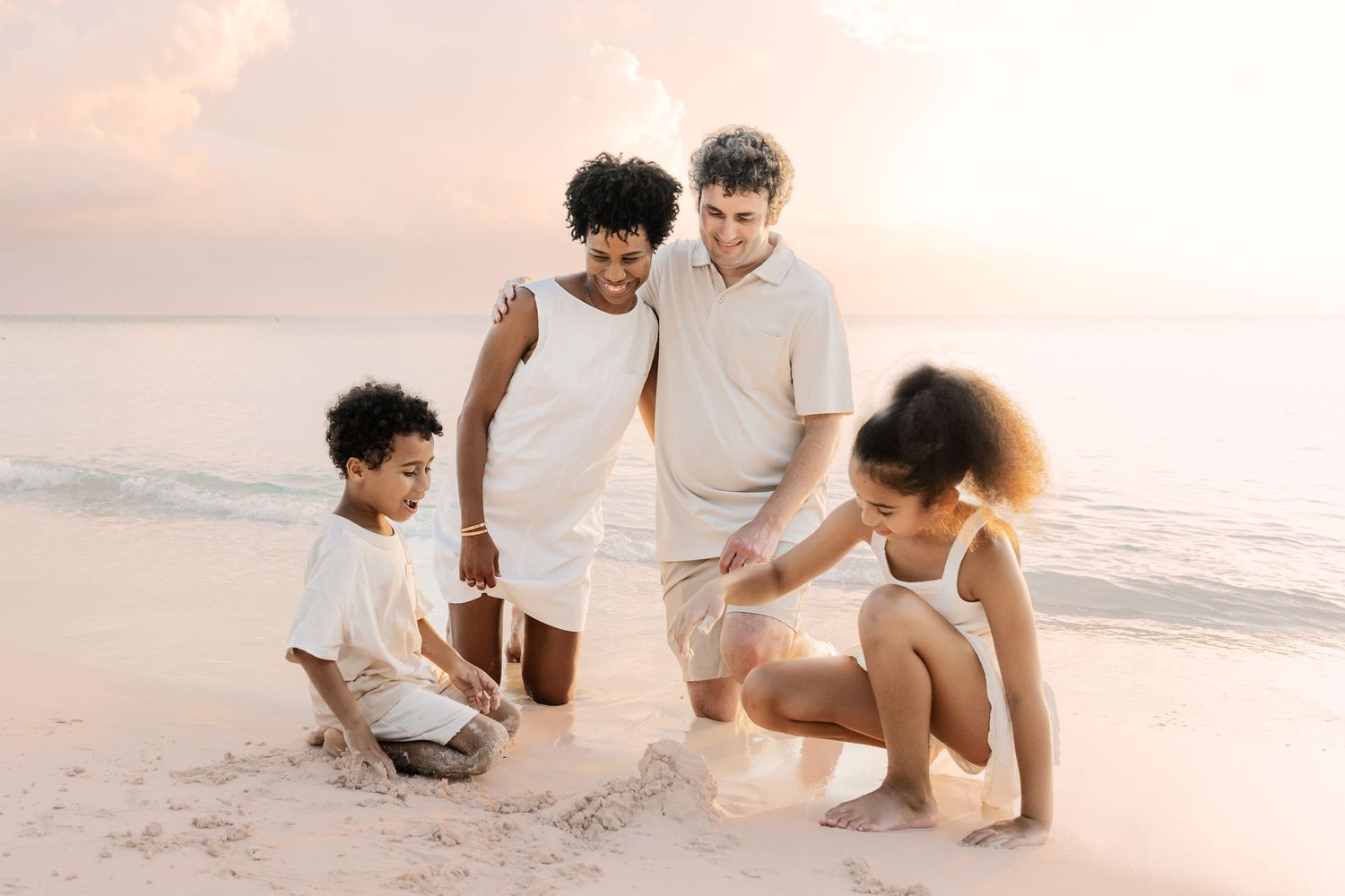 People in light colored clothing enjoying a casual moment together on a beach at sunset.