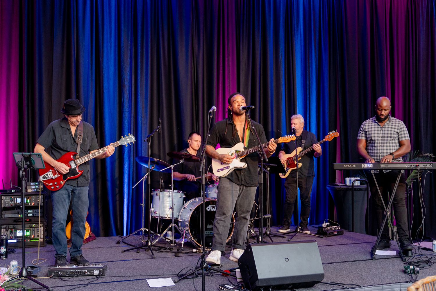 Live band performing on stage with colorful blue and purple lighting effects.