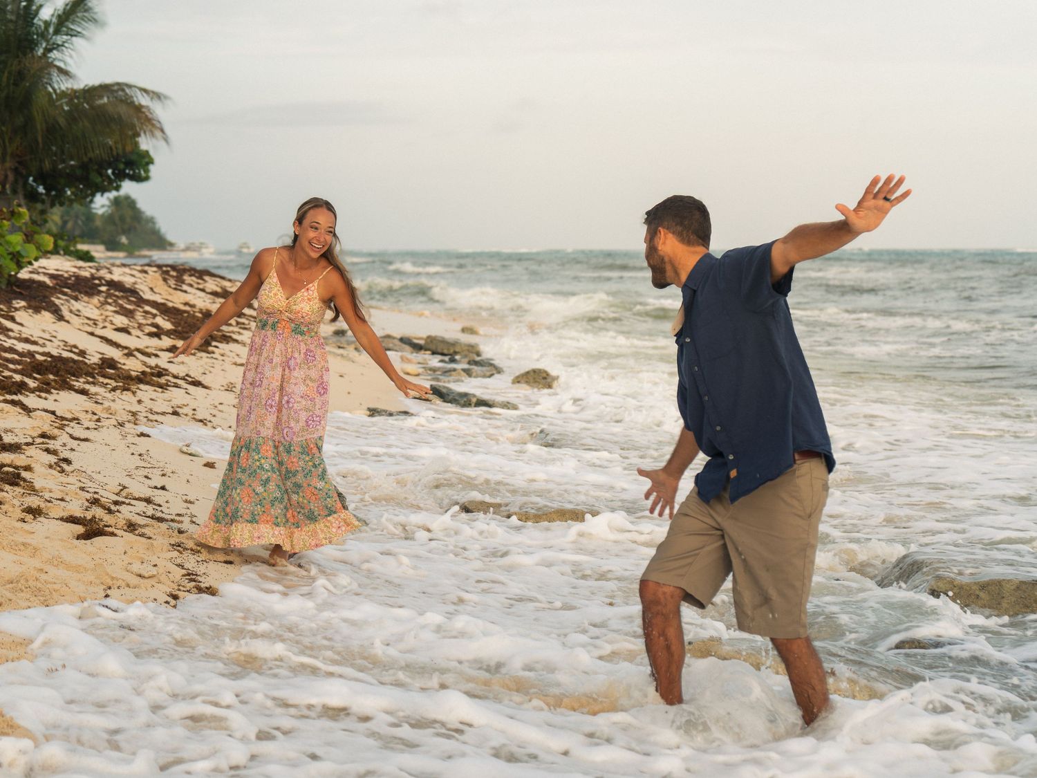 Couple playing in ocean waves at tropical beach during golden hour sunset.