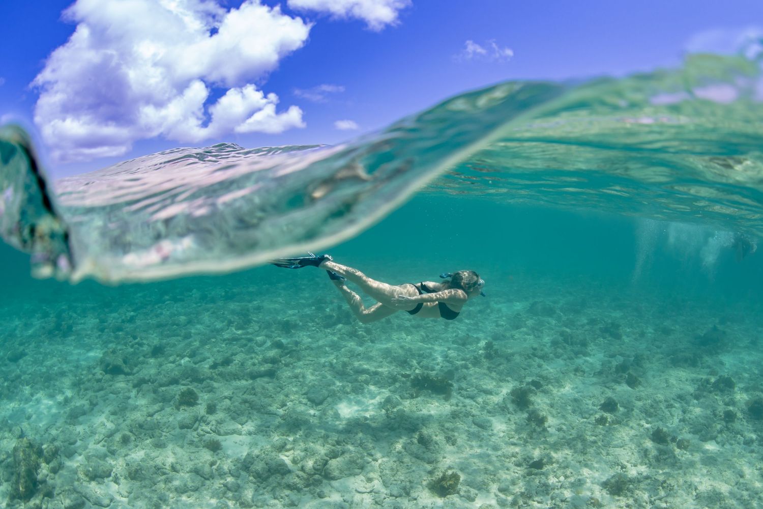 Split underwater view of snorkeler swimming in tropical waters with mountains visible above surface.