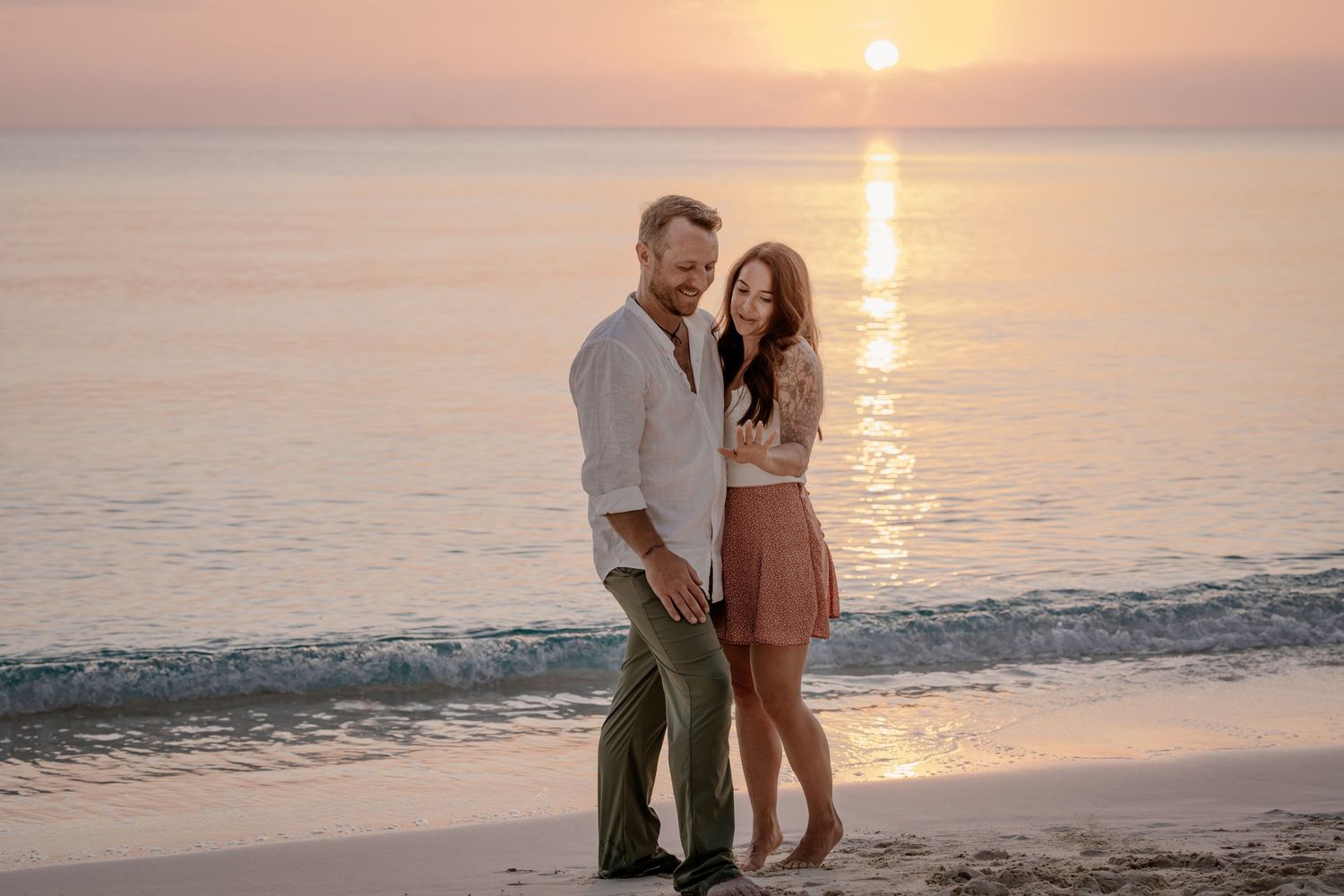 Couple walking along shoreline during golden sunset.