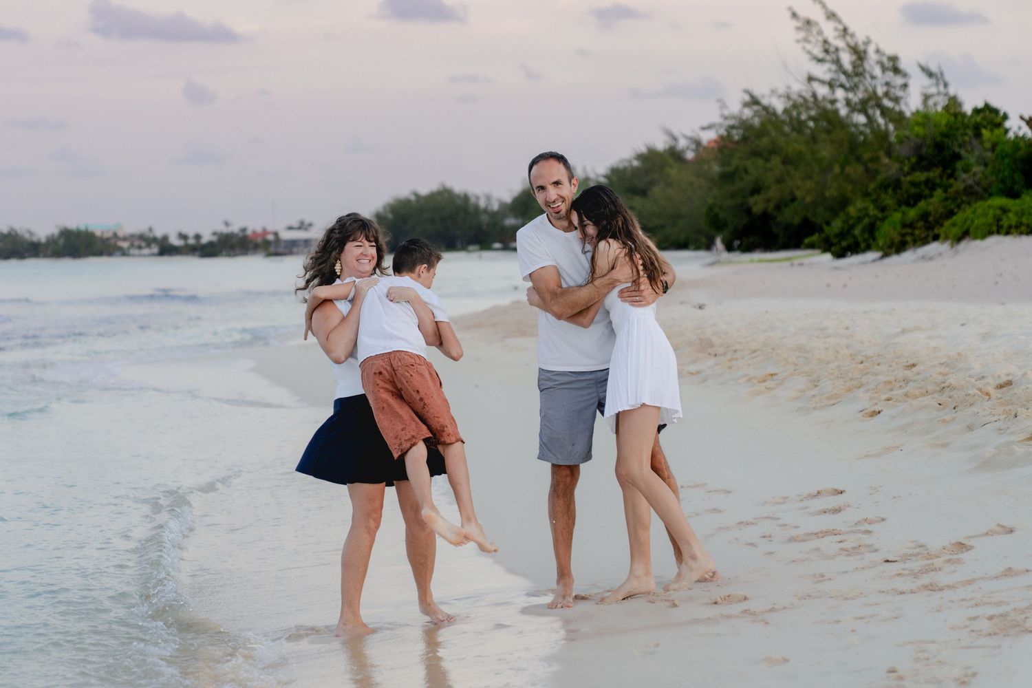 Playful family portrait on beach with people being carried and laughing.