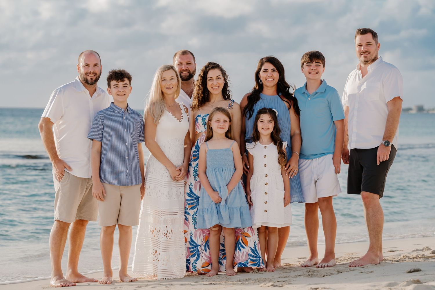 Extended family gathered for a professional beach portrait session in coordinated blue and white outfits.