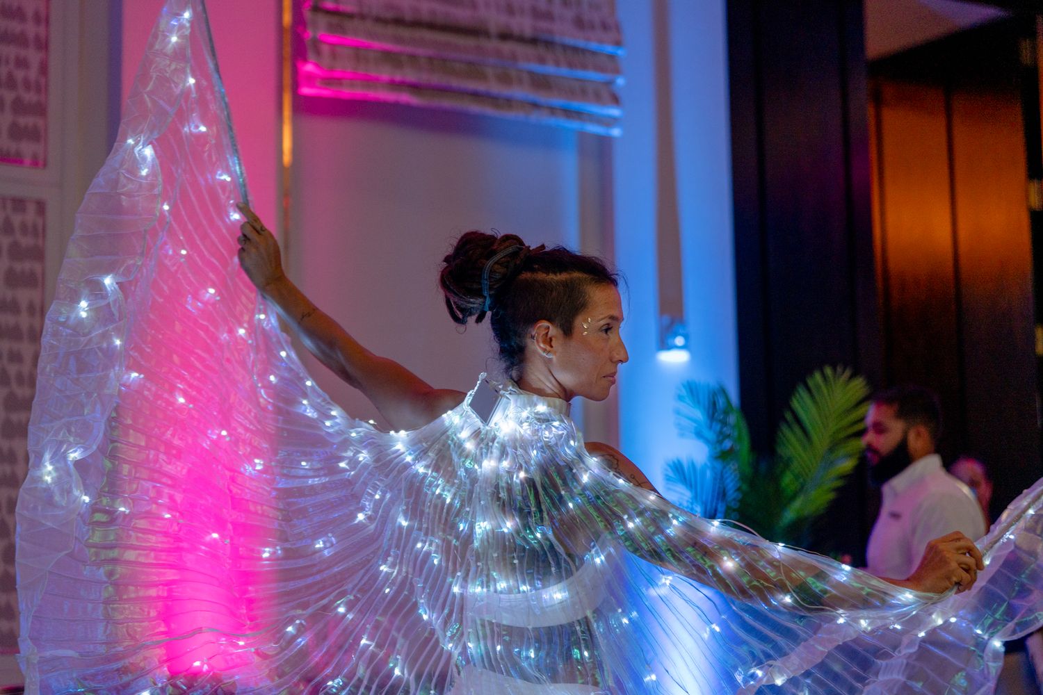 Dancer with glowing LED wings creates dramatic silhouette against colorful stage lighting.