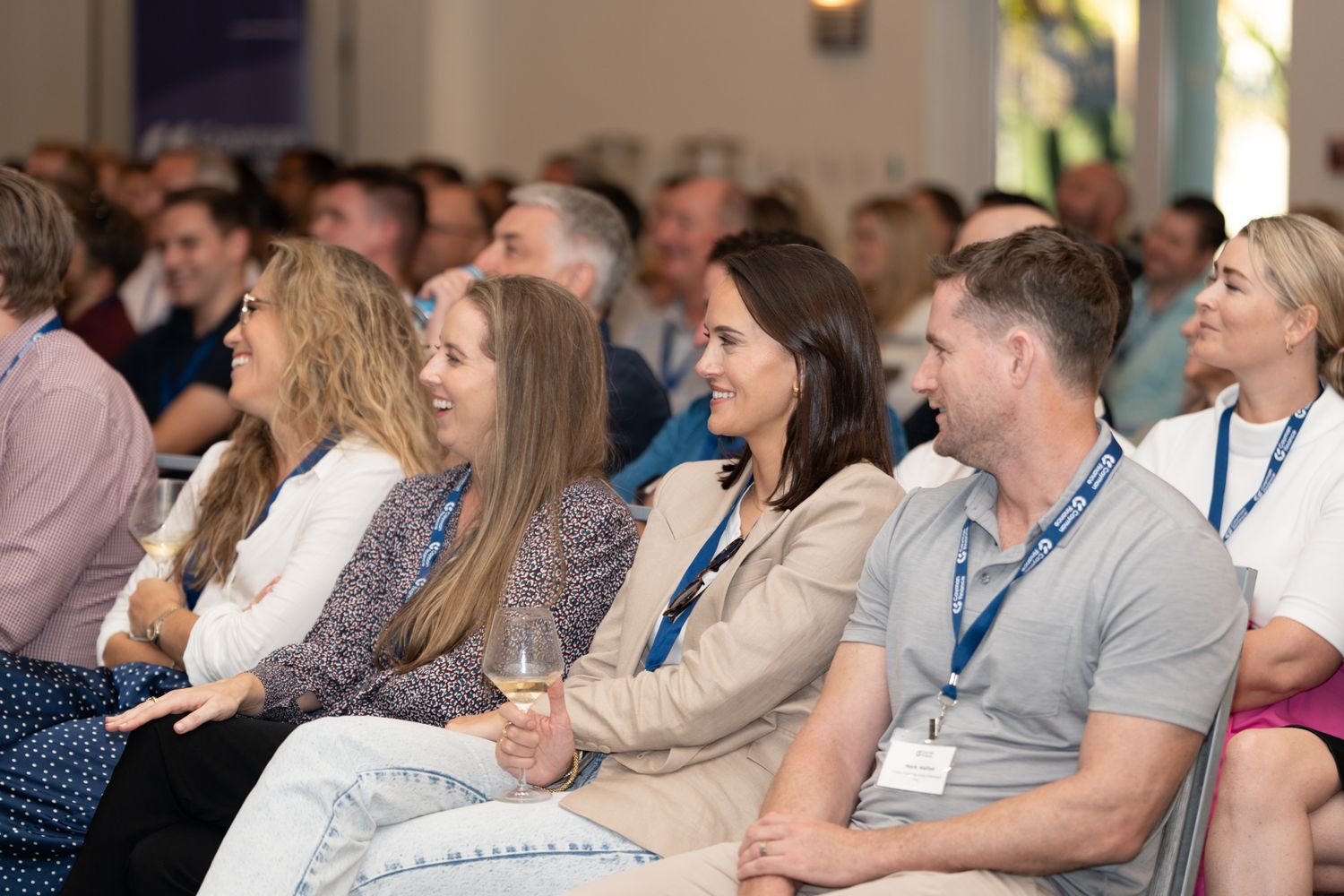 Conference attendees seated in rows listening attentively to a presentation in a well-lit venue.