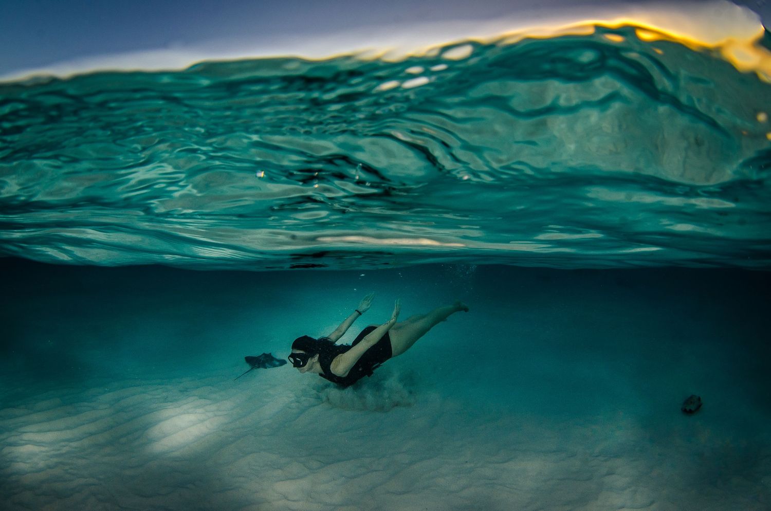 Split underwater view shows tranquil ocean surface meeting deep blue waters.