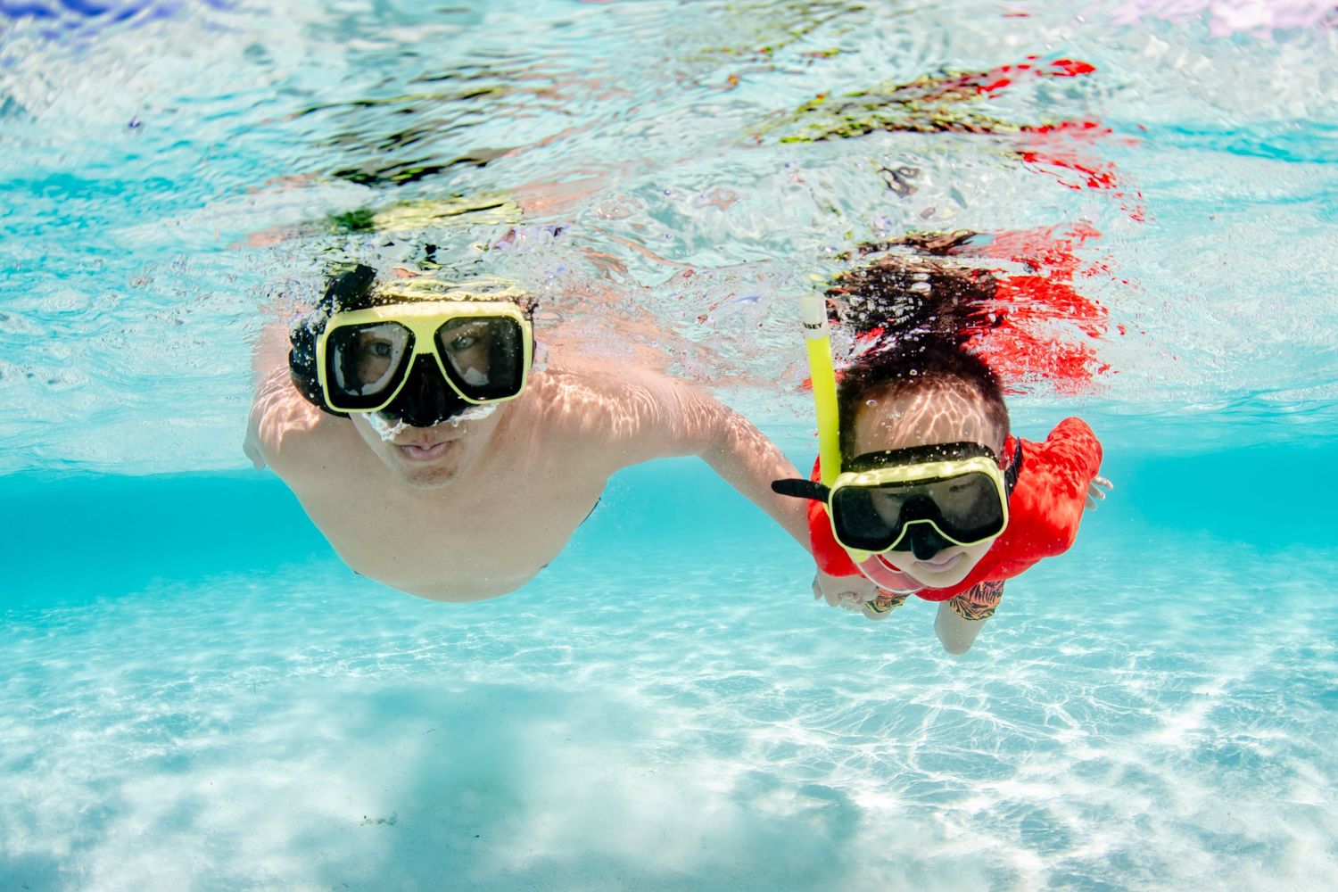 Snorkelers swimming underwater in crystal clear turquoise ocean.
