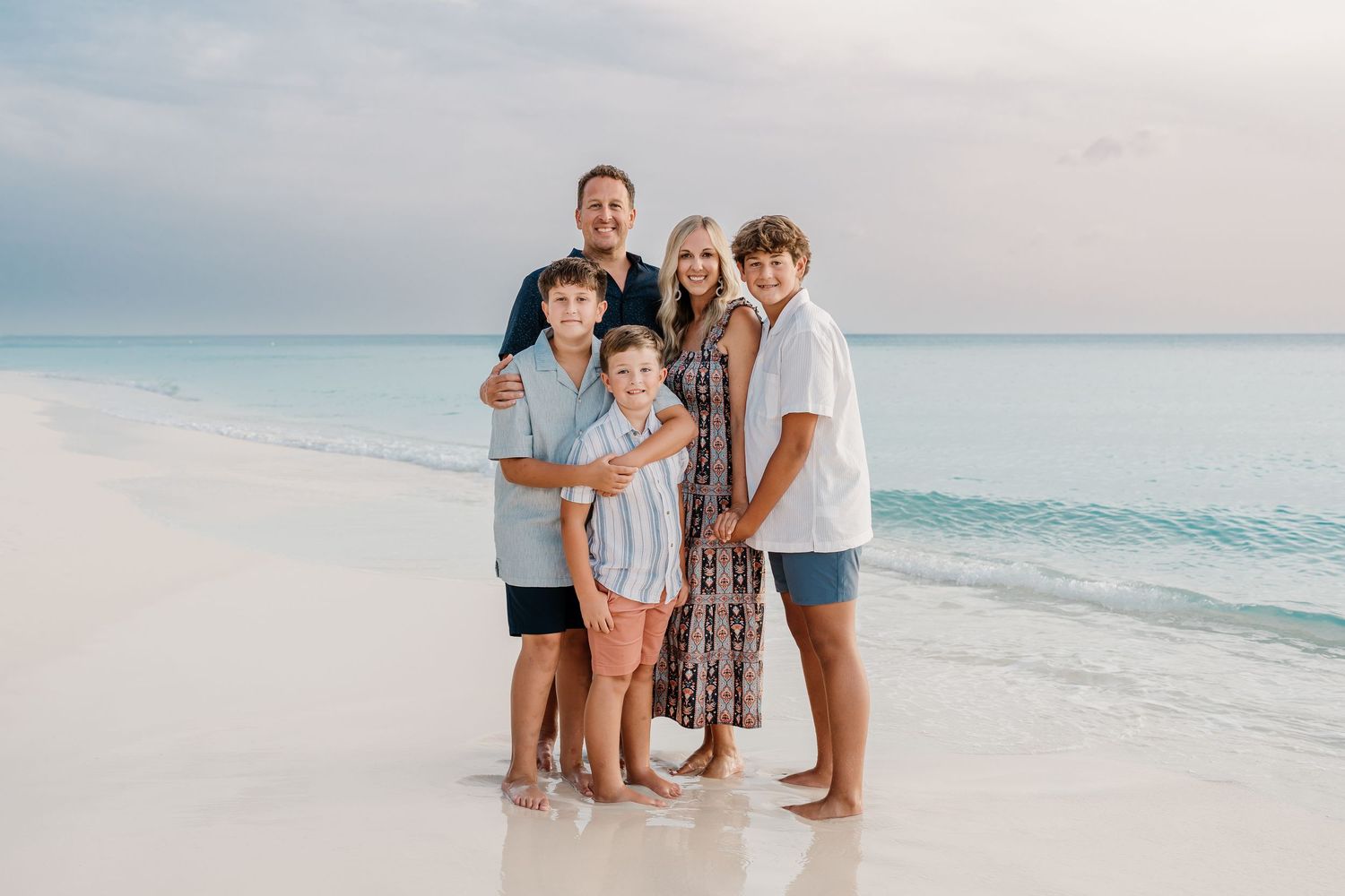 Family enjoying a sunset photoshoot on a pristine white sand beach with turquoise ocean waves in the background.