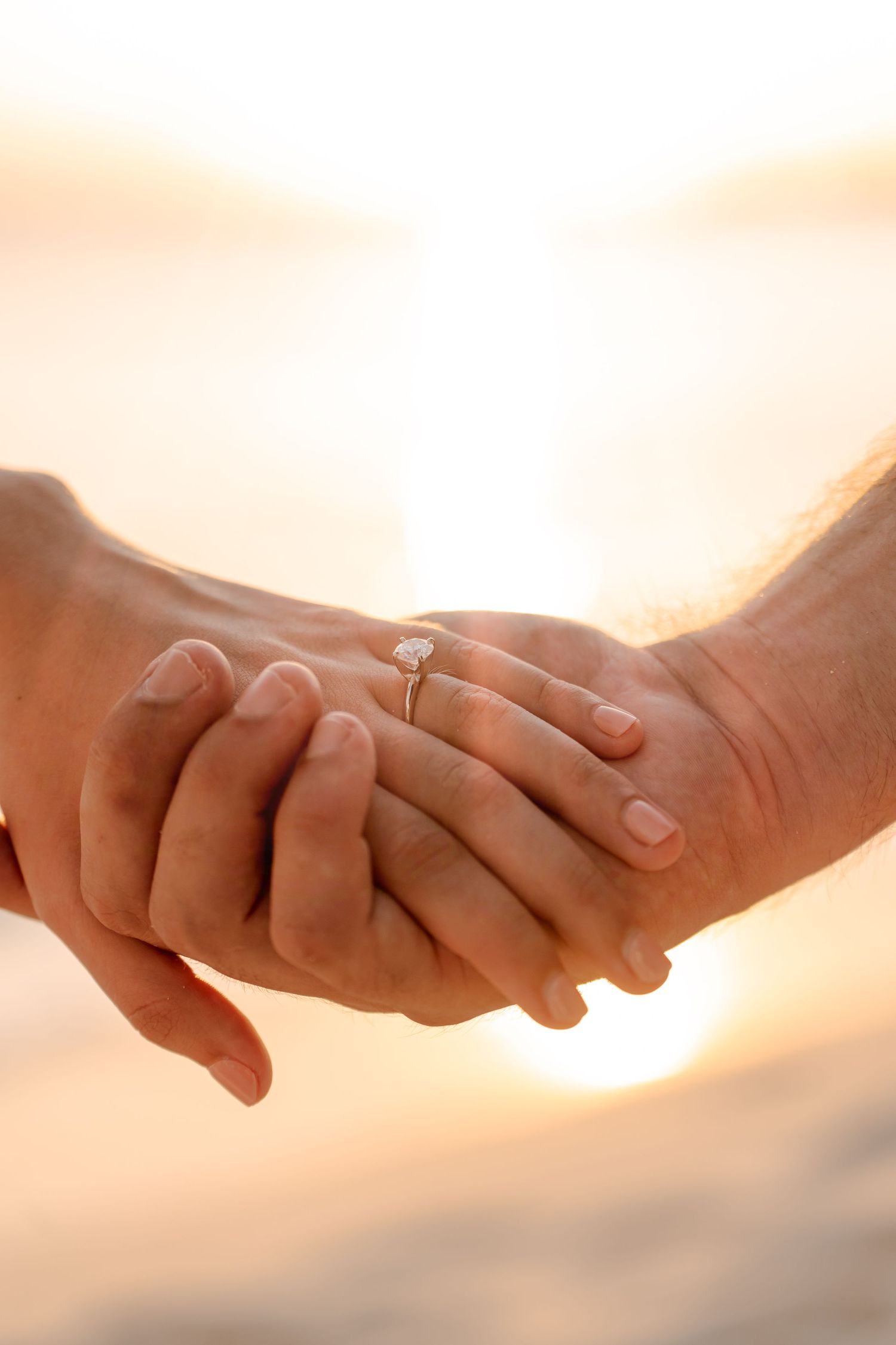 Hands intertwined against sunset backdrop showing wedding rings.