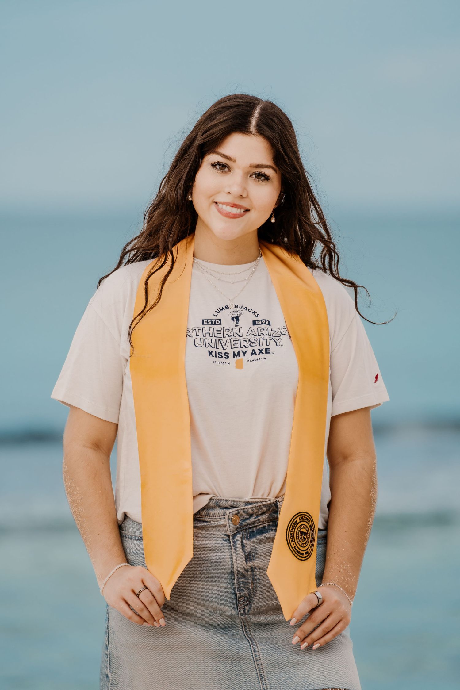 Woman wearing yellow vest and graphic tee poses by ocean.