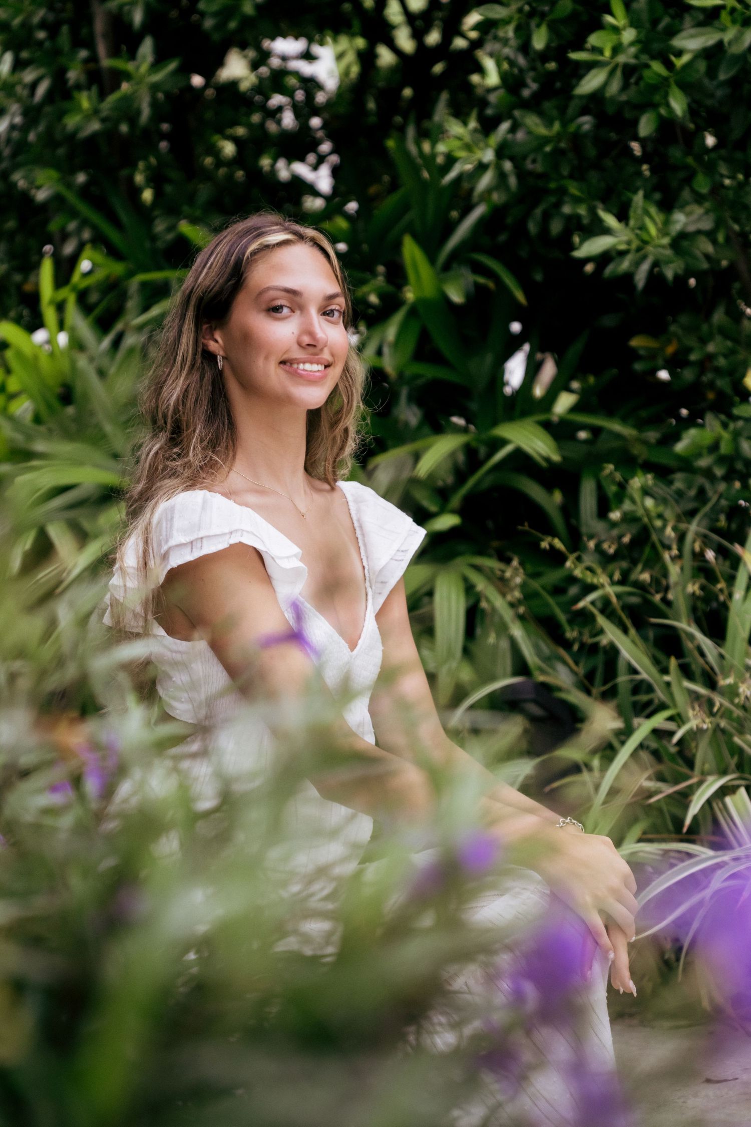 A summer portrait framed by lush green foliage and purple flowers in soft focus.