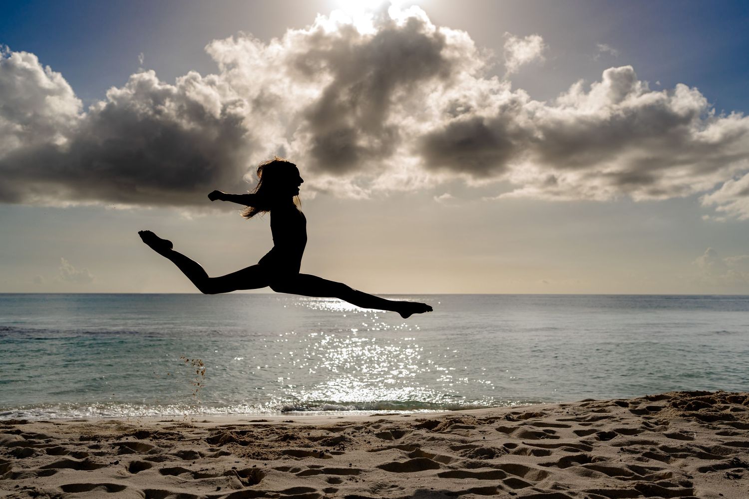 Silhouette of person jumping at beach during dramatic sunset.
