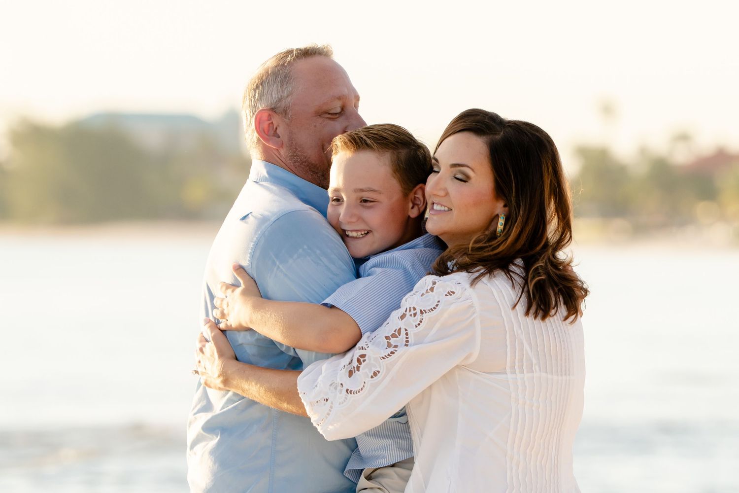 Family members share warm embraces on a bright beach during a photo session.