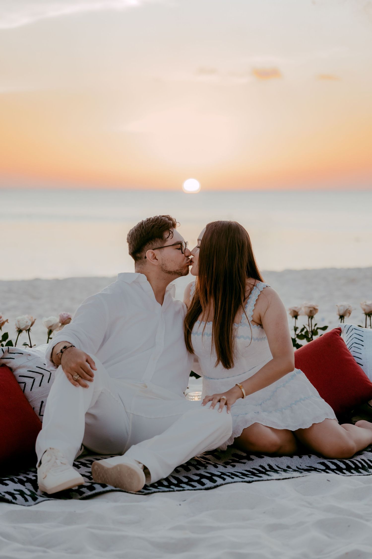 Romantic couple lounging on beach blanket at sunset over ocean horizon.