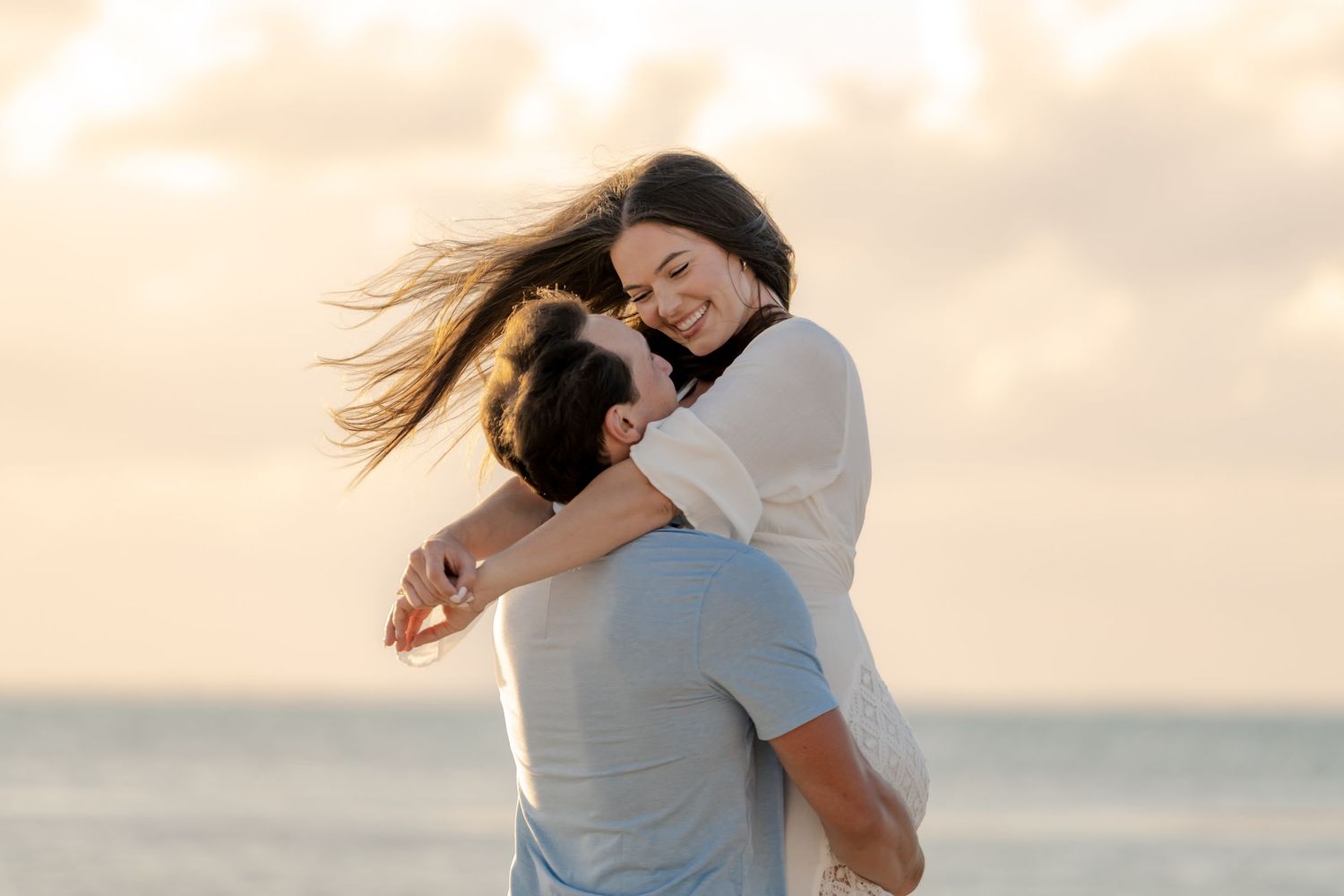 Playful embrace on beach during golden hour with ocean backdrop.