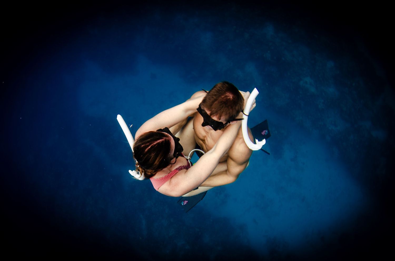 Underwater view of snorkeler diving in dark blue ocean waters.