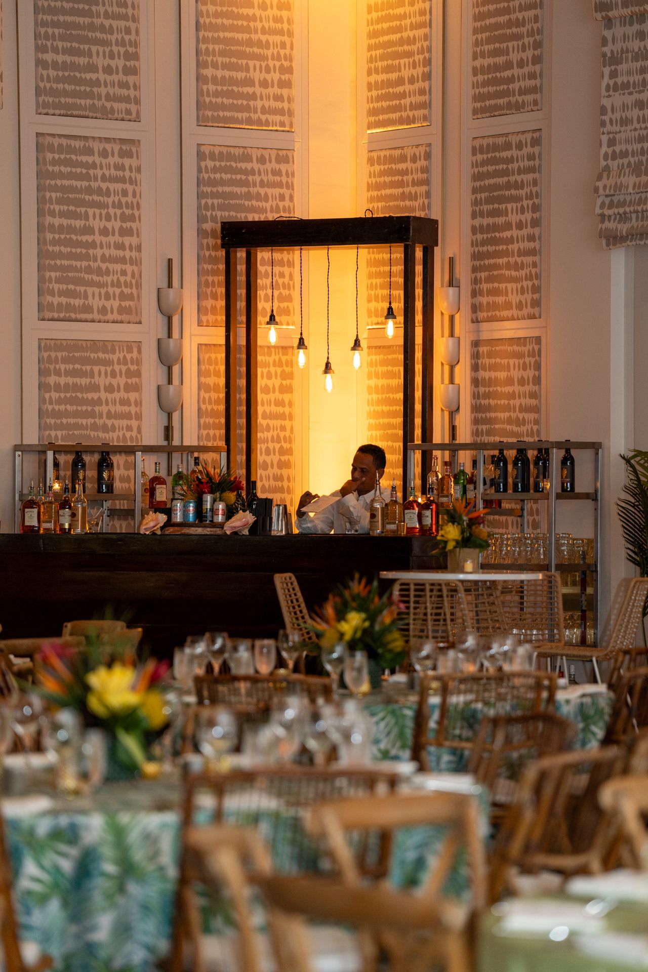 Warm-lit bar setup in an elegant venue with text-covered walls and hanging pendant lights.