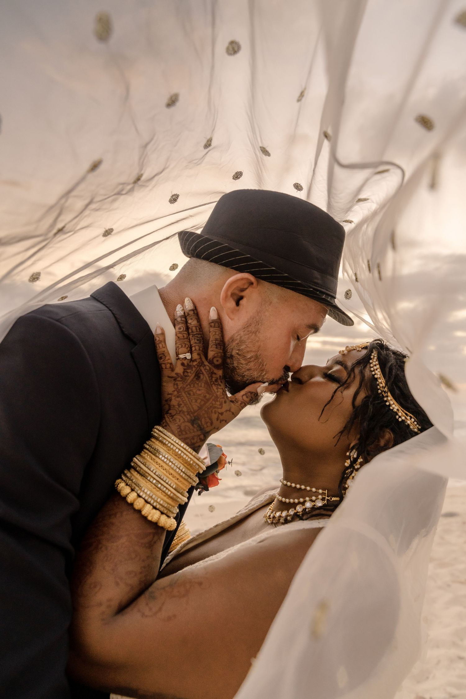 Wedding couple shares romantic kiss under decorative lighting with traditional henna details.